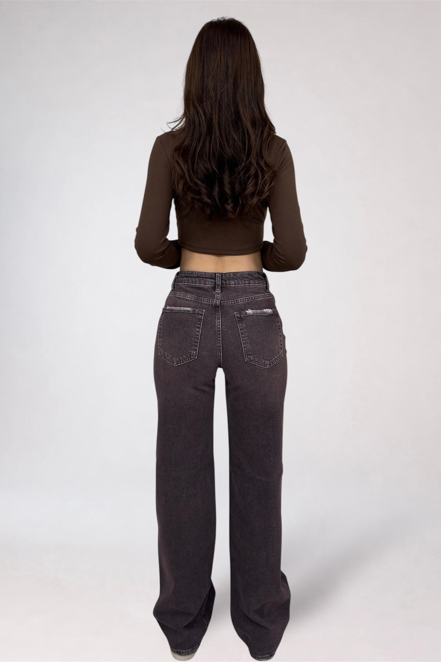 Person wearing dark jeans and a brown long-sleeve top on a white background