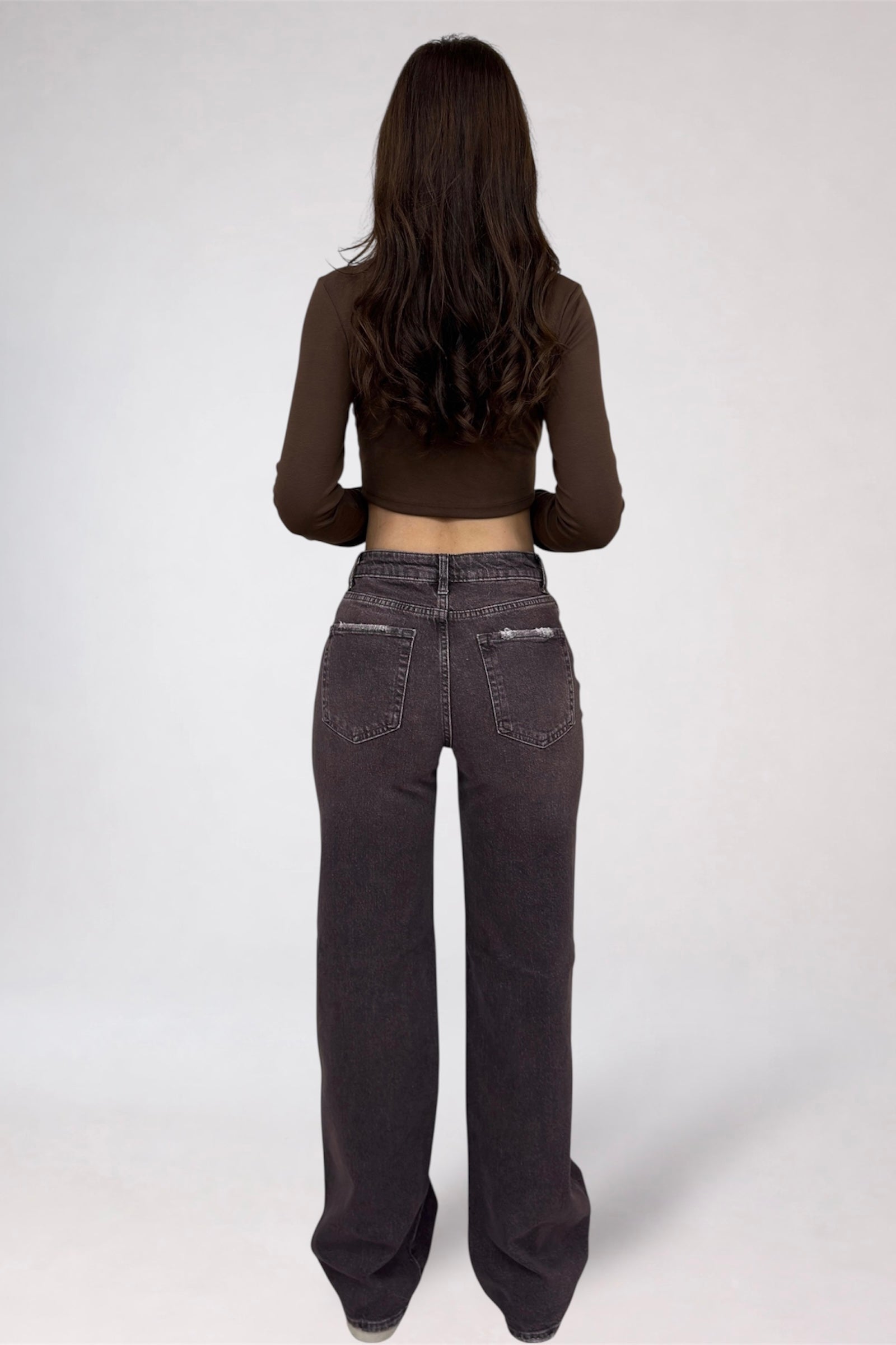 Person wearing dark jeans and a brown long-sleeve top on a white background