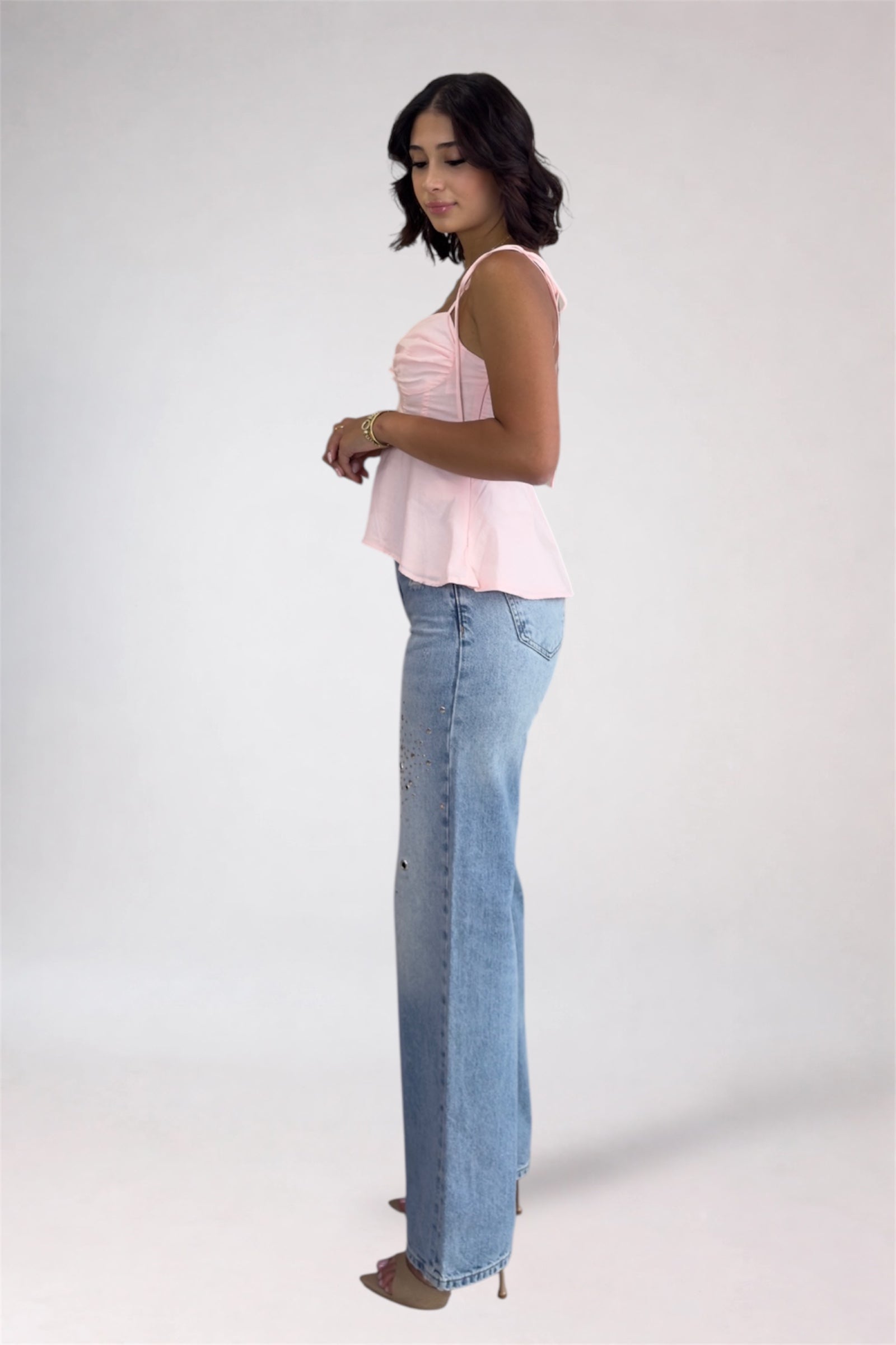 Woman wearing a light pink top and blue jeans on a white background