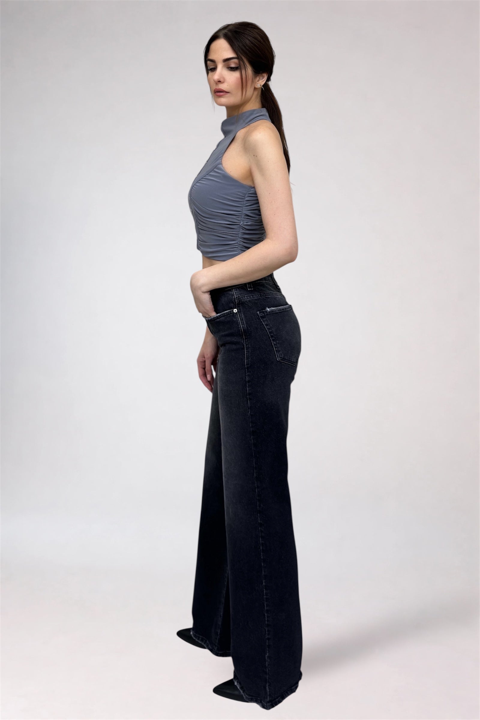 Woman wearing a gray top and black flared jeans on a white background