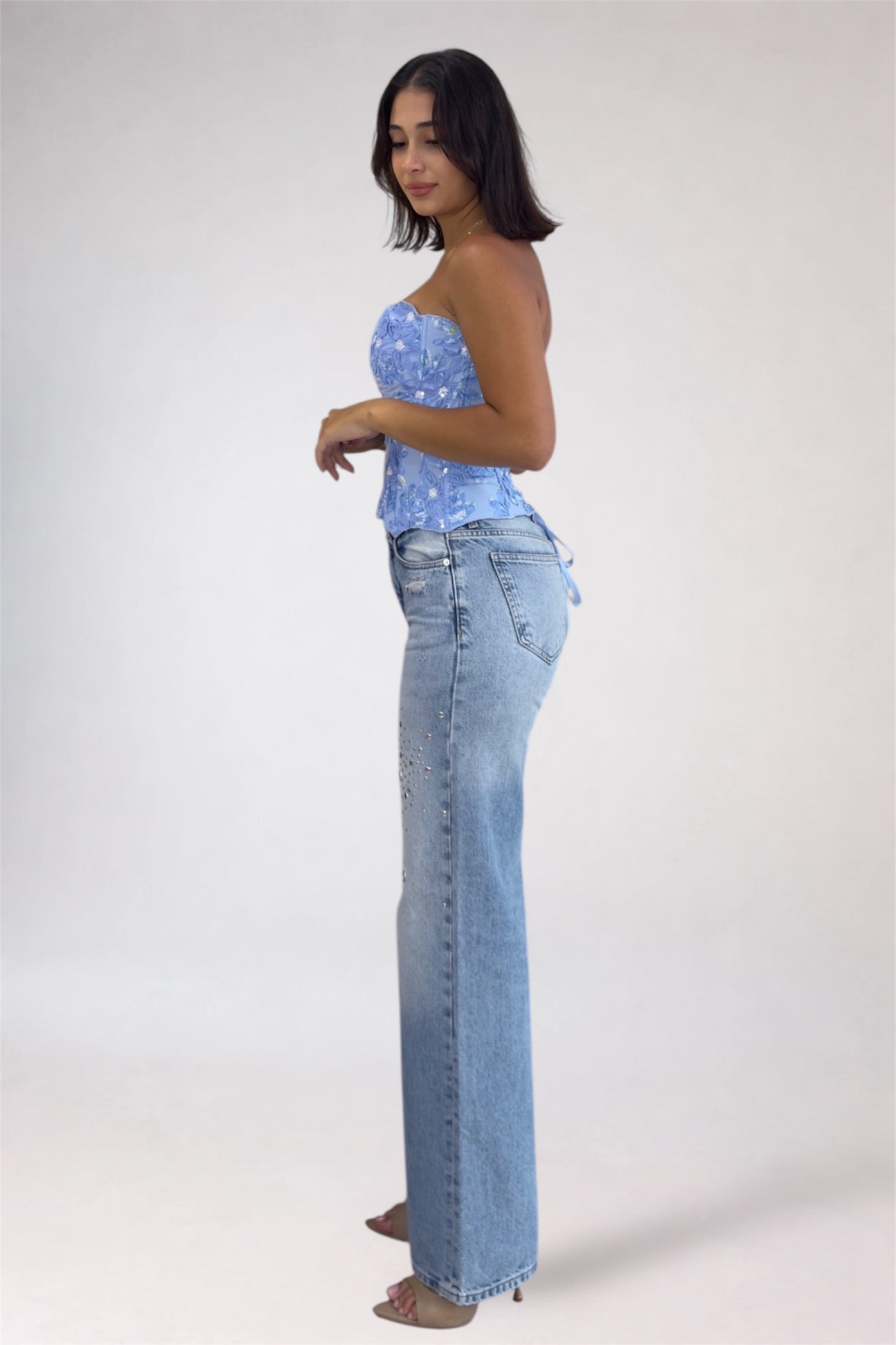 Woman wearing a blue strapless top and light blue jeans on a white background