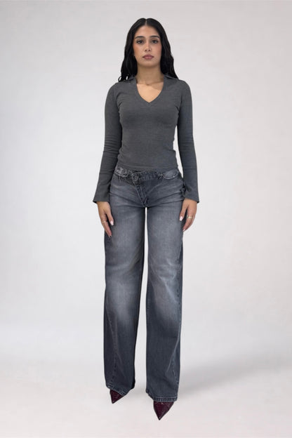 A woman modeling a dark gray long-sleeve V-neck top and wide-leg gray jeans against a plain light gray studio background.