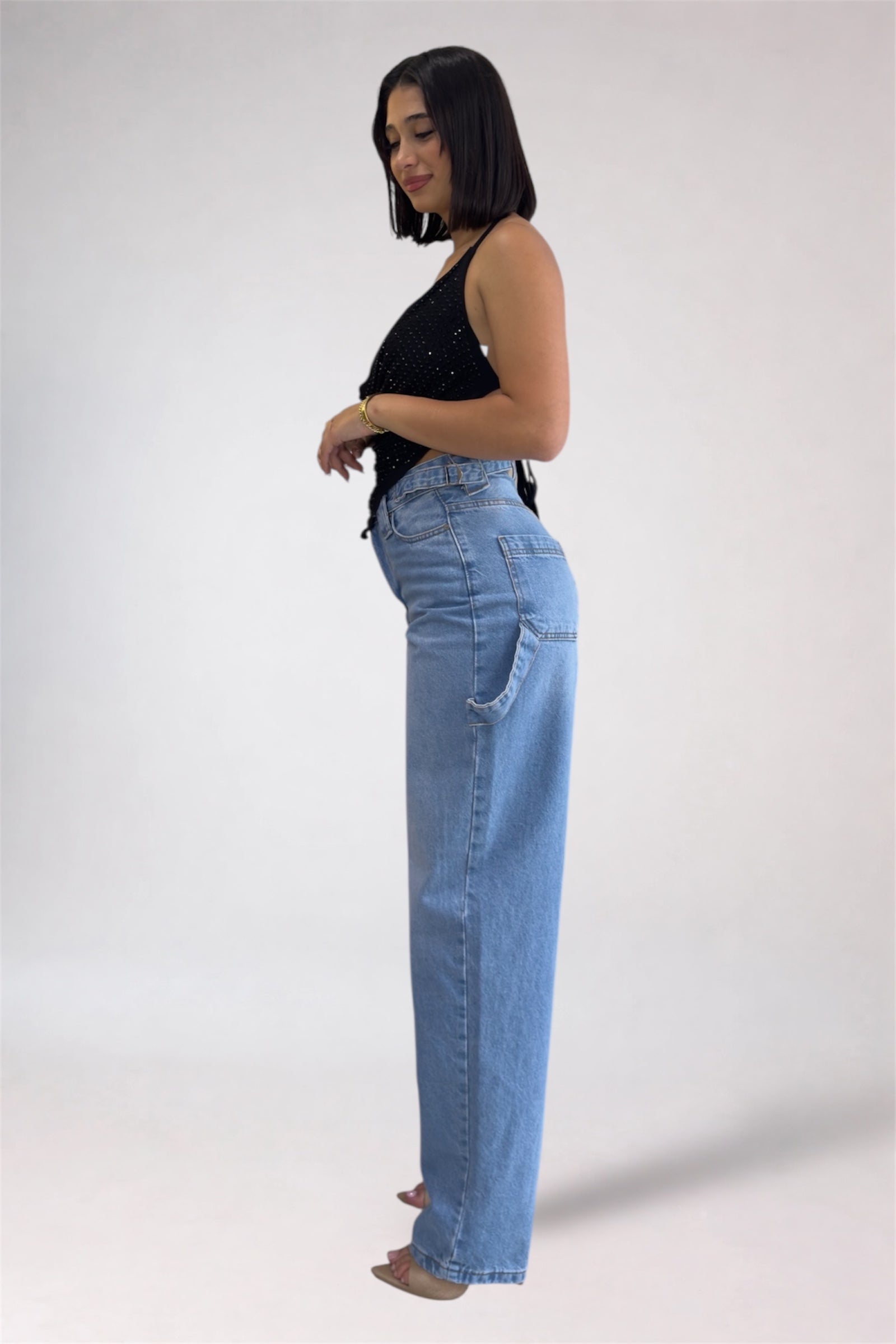 Woman wearing light blue jeans and a black top on a white background