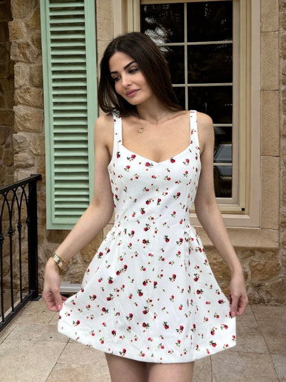 Woman wearing a white dress with red floral pattern standing in front of a stone building.