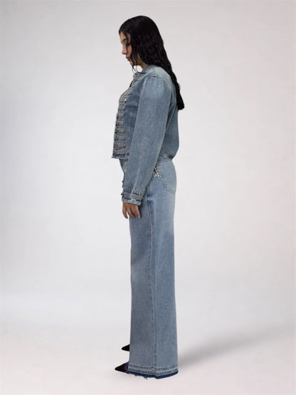 A model shown from the side profile wearing a matching light-wash denim set consisting of a cropped denim jacket and wide-leg denim pants, set against a plain light gray studio background.
