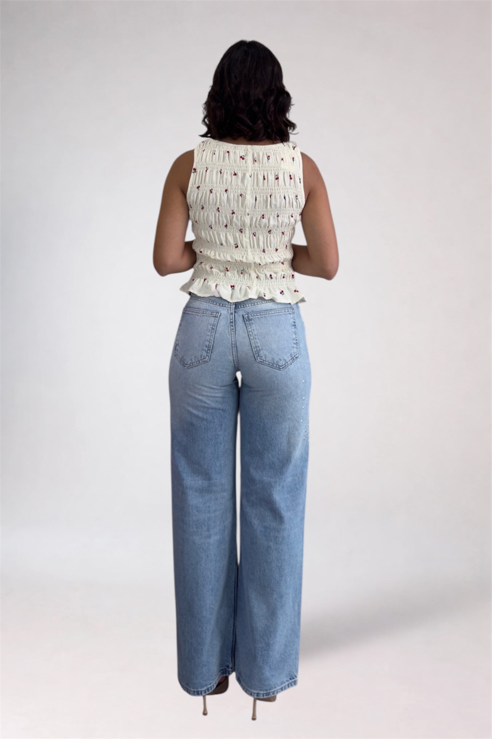 Person wearing a white sleeveless top and blue jeans on a plain background