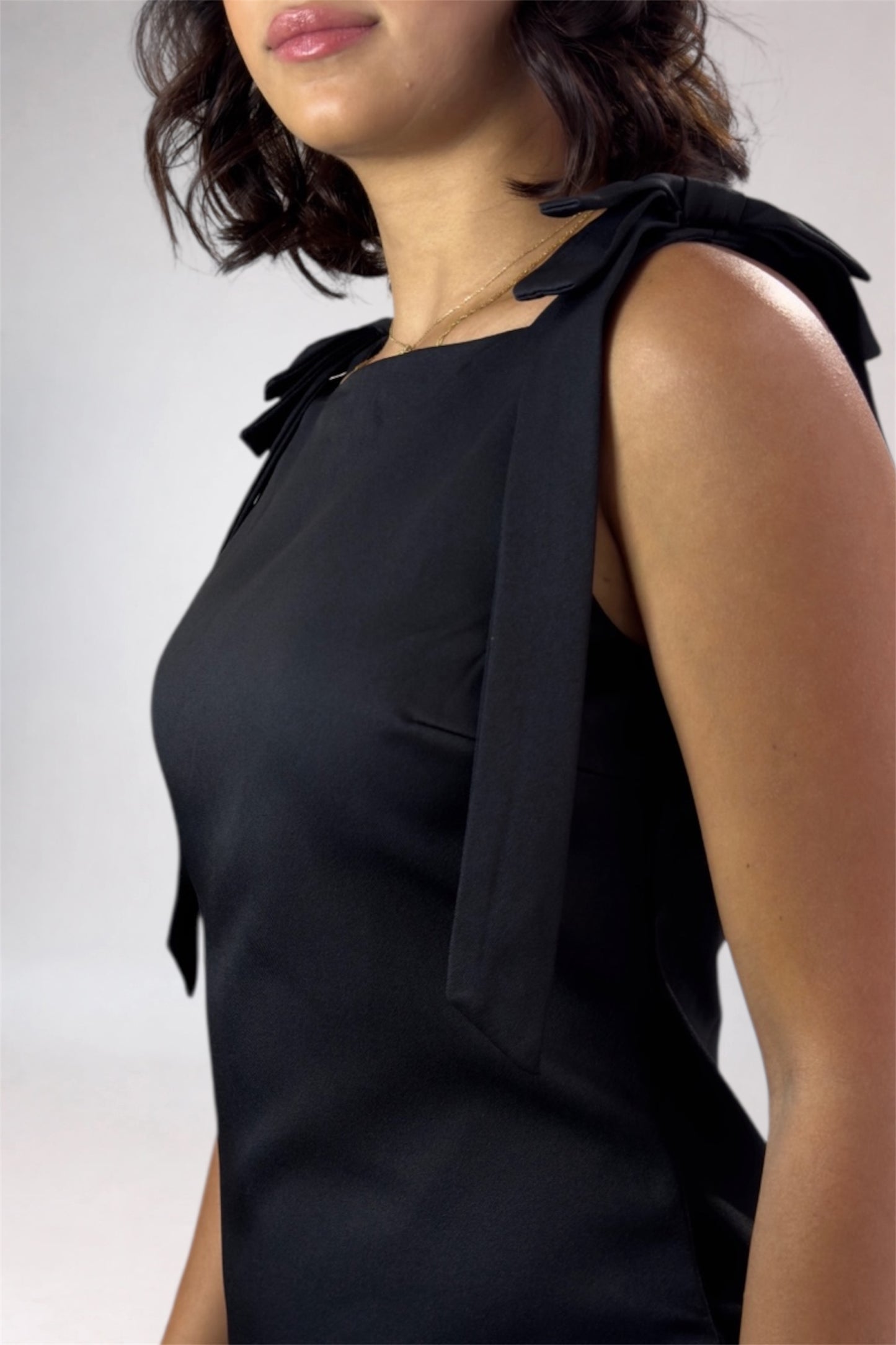 Black sleeveless top with bow details on a plain background
