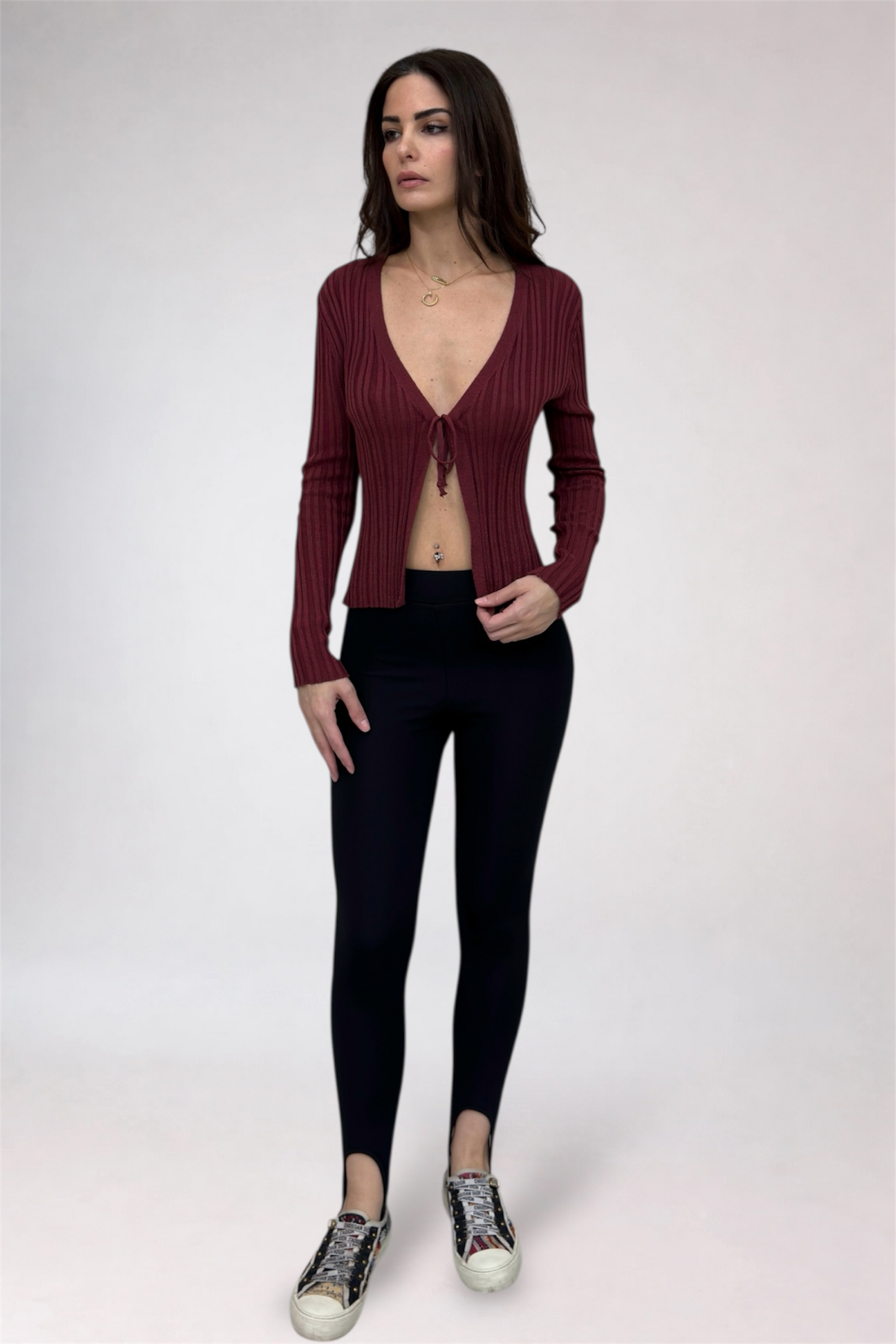 Woman wearing a maroon ribbed sweater and black leggings on a white background