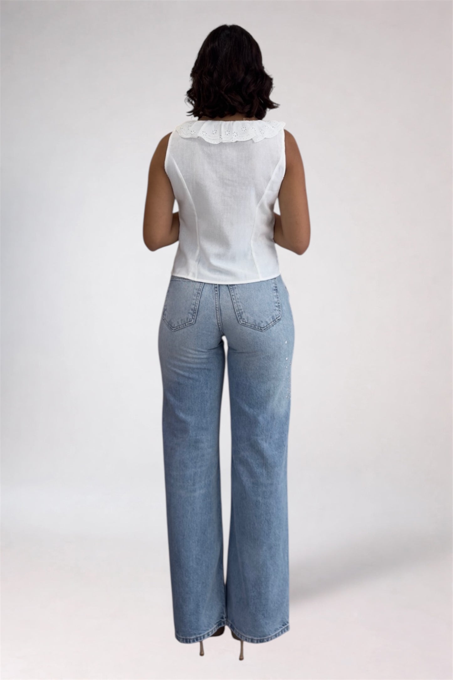 Person wearing a white sleeveless top and light blue jeans on a plain background