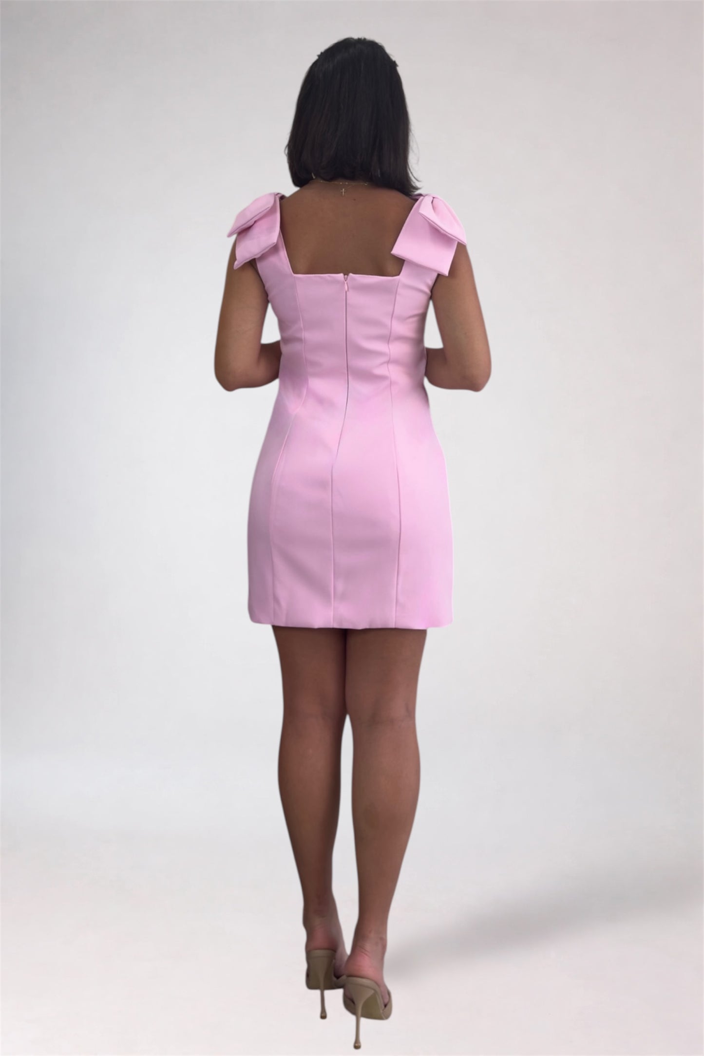 Pink dress with bow straps worn by a person on a white background