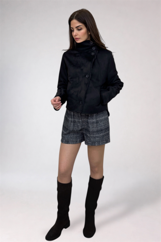 Woman wearing a black jacket, gray shorts, and black knee-high boots on a white background