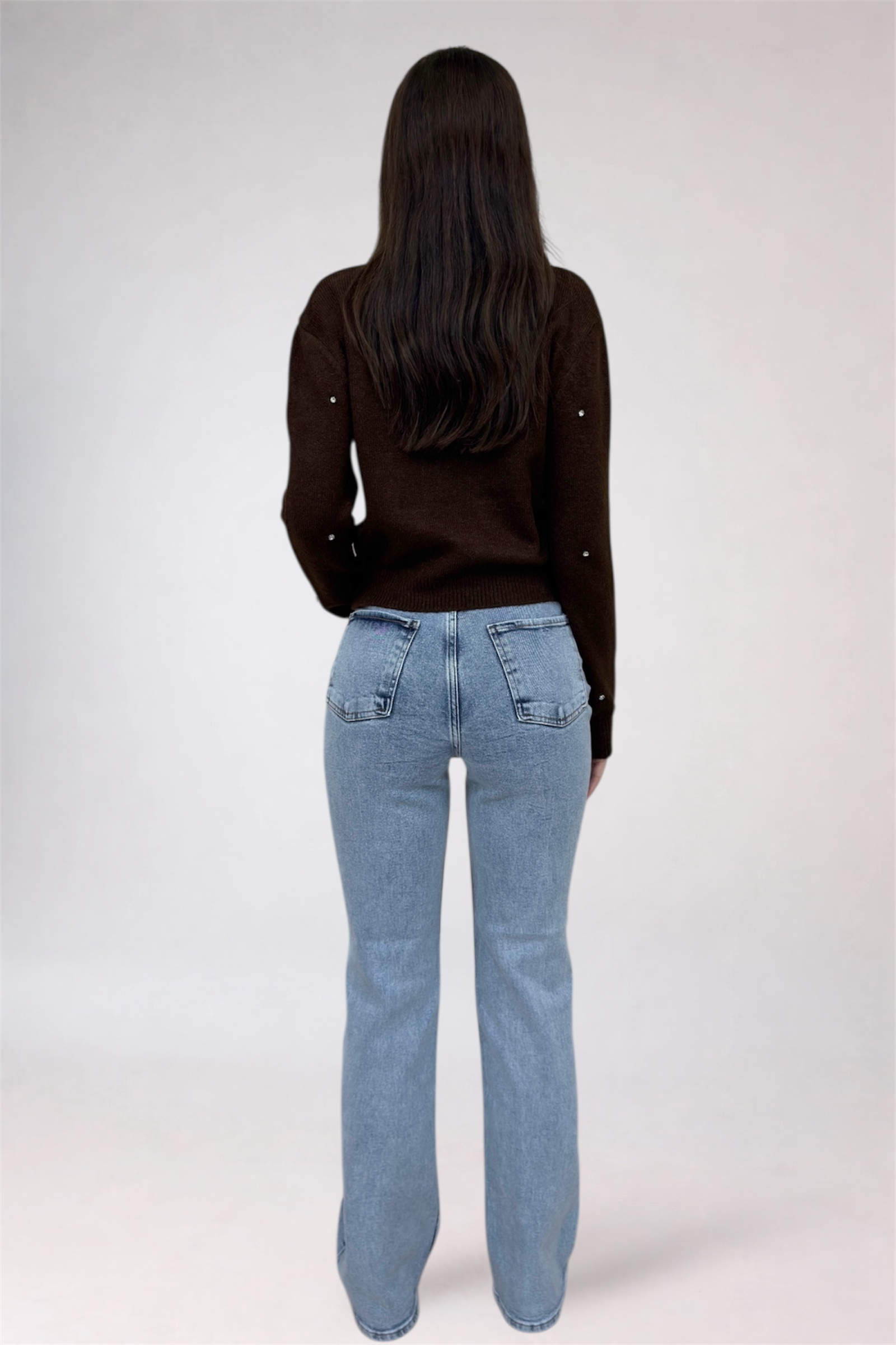 Person wearing a black long-sleeve shirt and light blue jeans on a white background