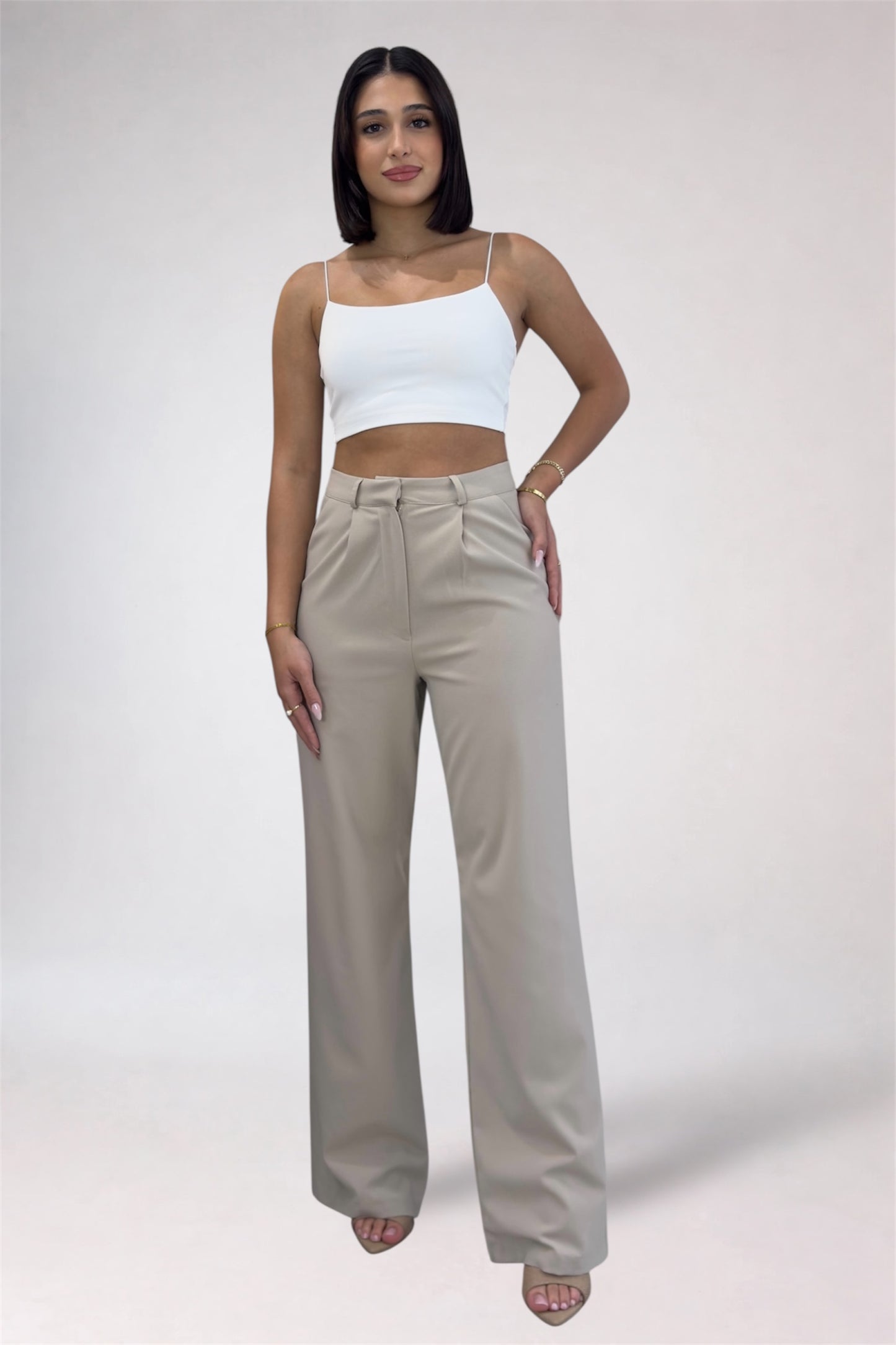 Woman wearing a white top and beige high-waisted pants on a plain background