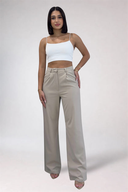 Woman wearing a white top and beige high-waisted pants on a plain background
