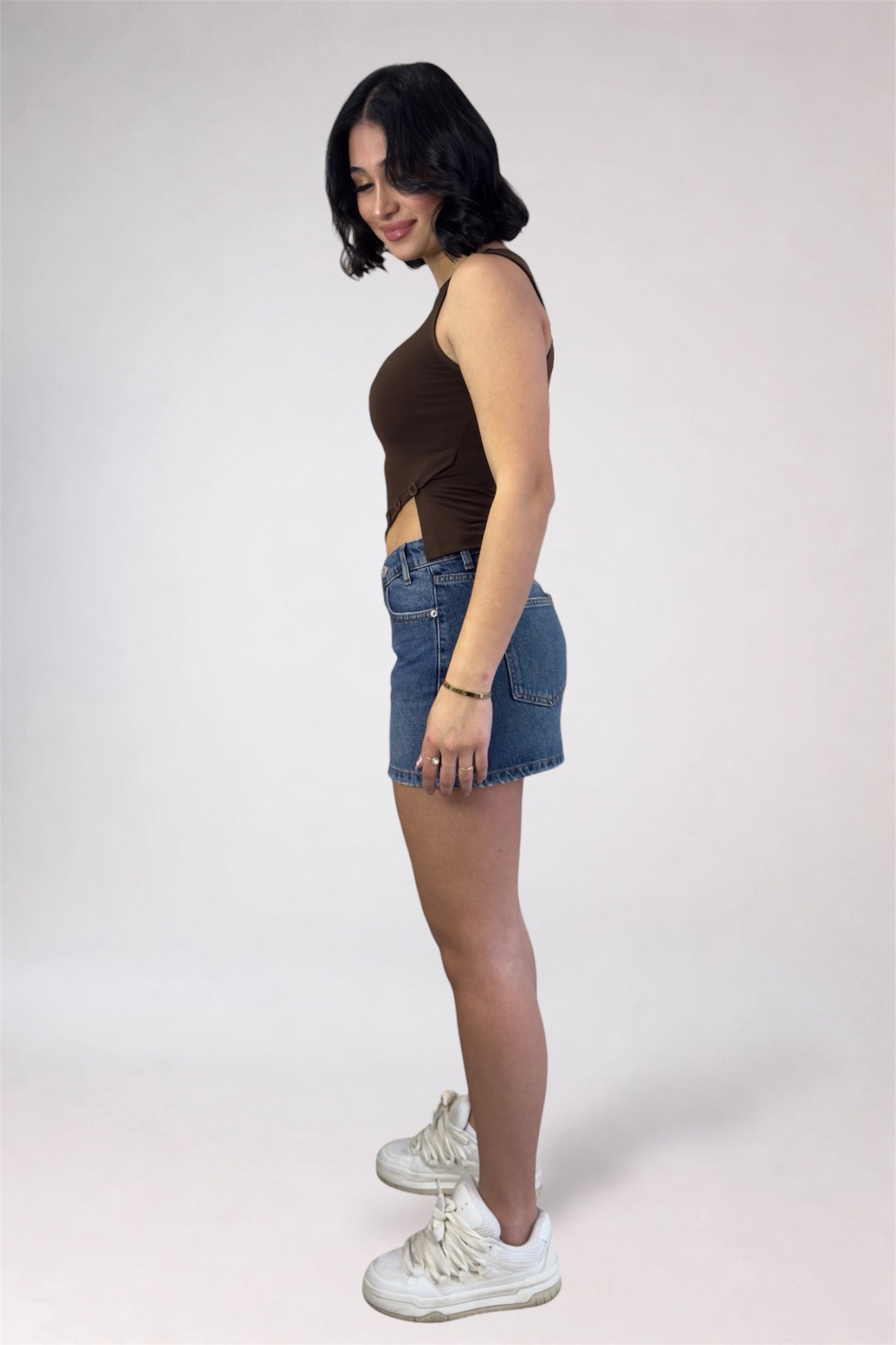Woman wearing a brown sleeveless top and denim shorts on a white background