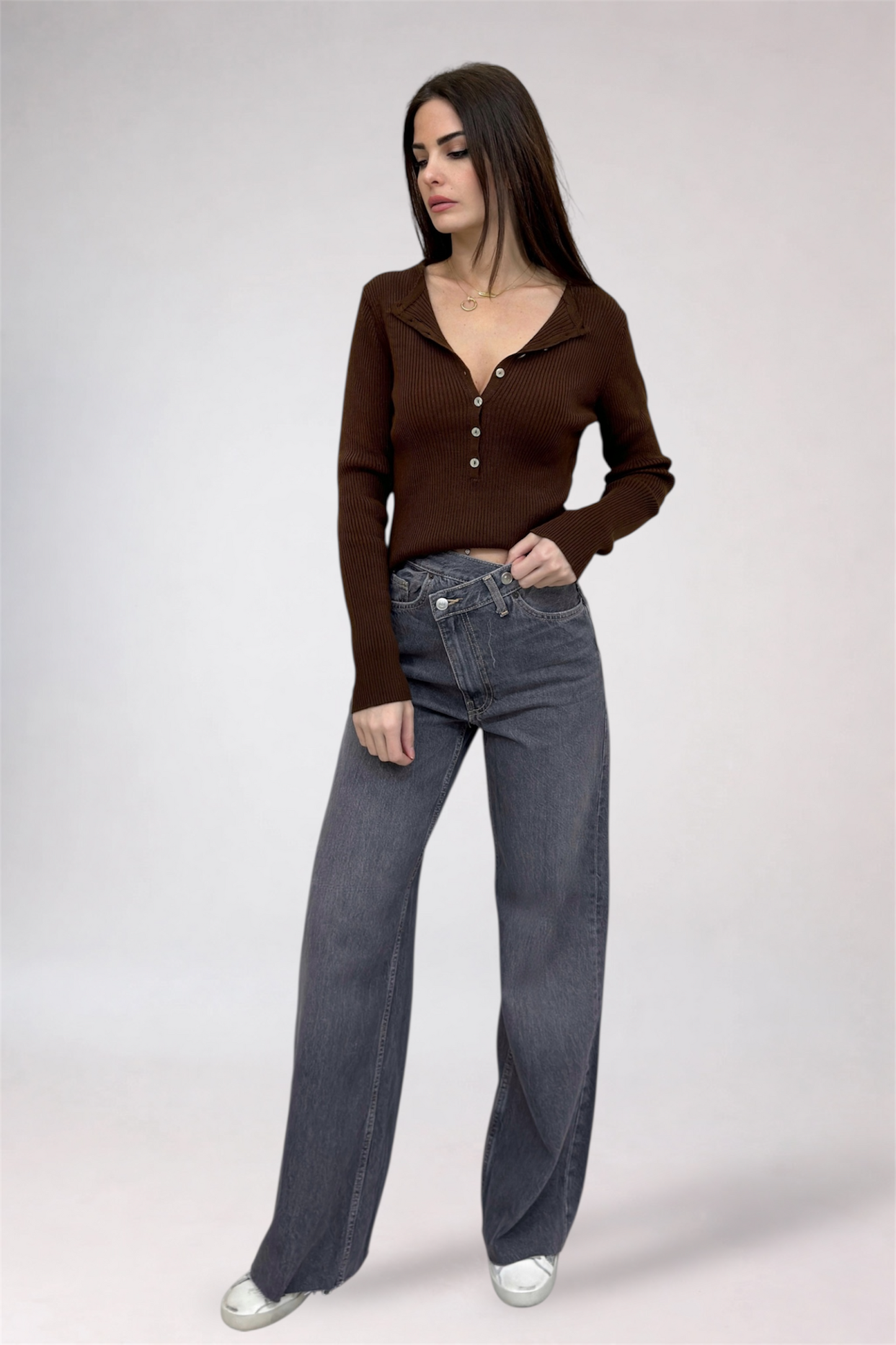 Woman wearing a brown long-sleeve top and gray jeans on a white background