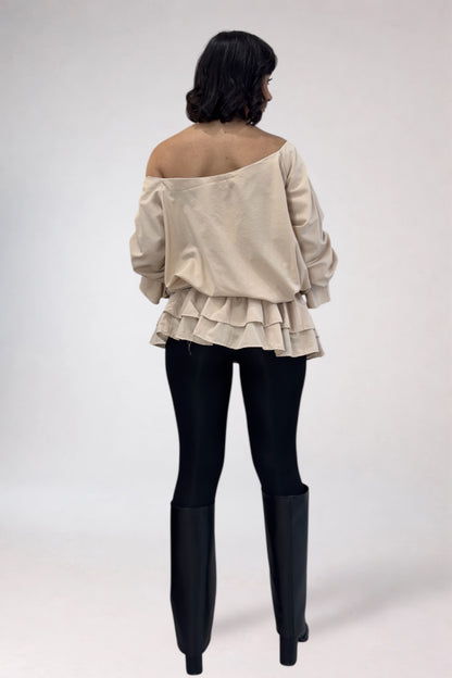 Woman wearing a beige off-shoulder top and black leggings with black boots on a white background