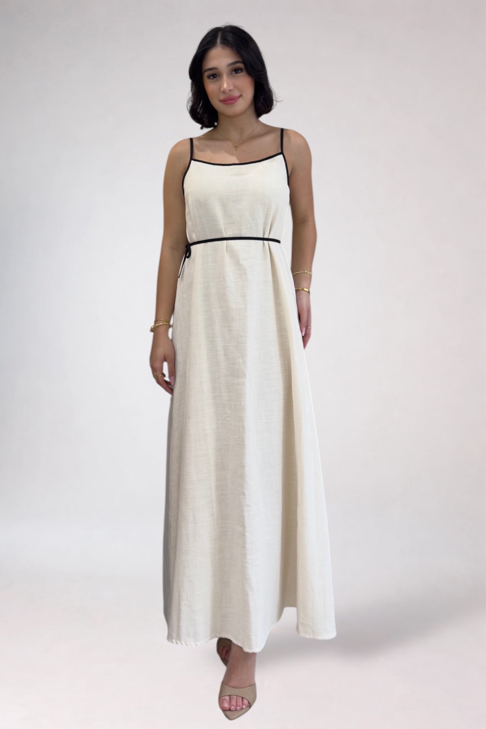 Woman wearing a white dress with black straps on a plain background