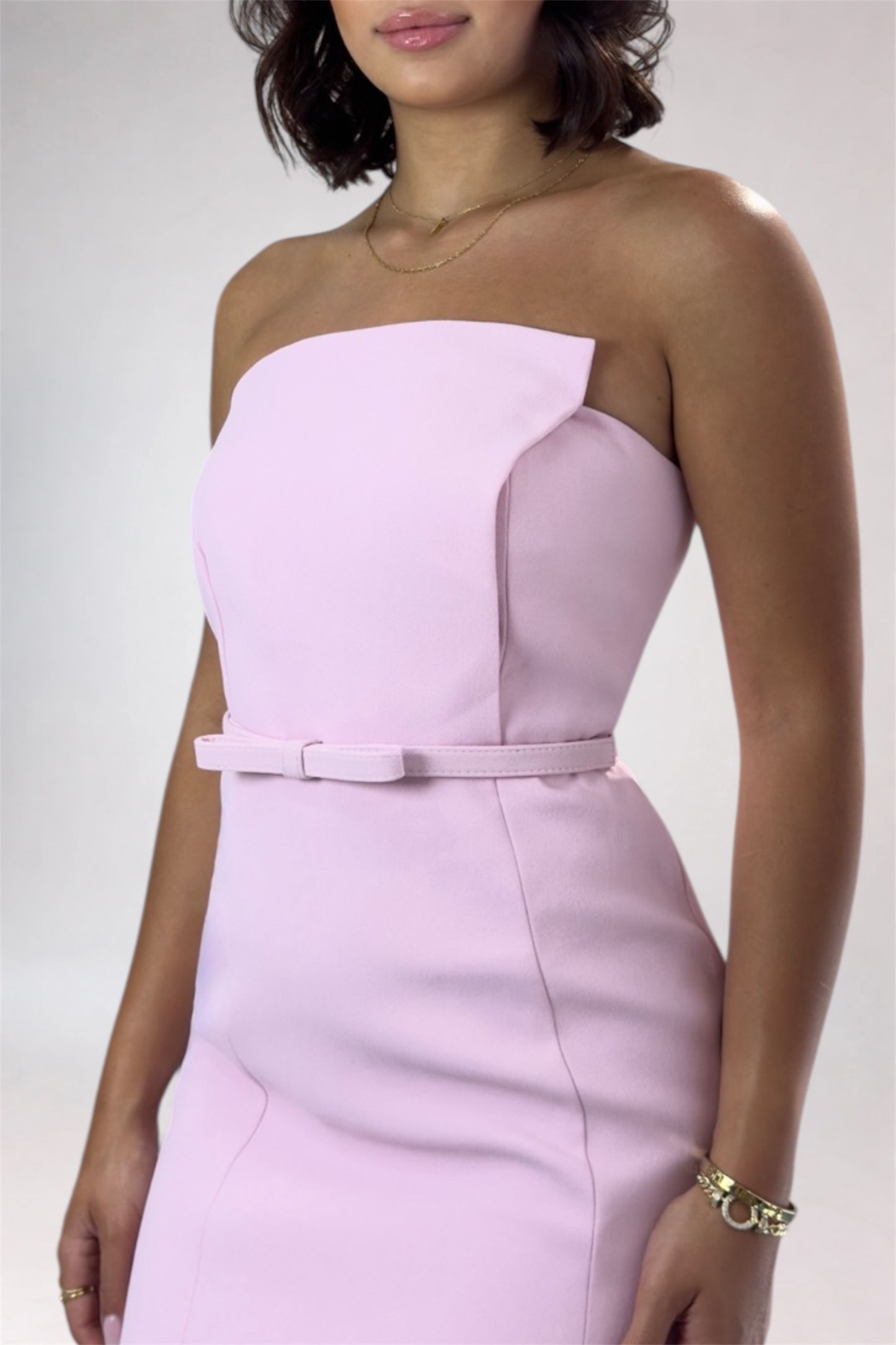 Woman wearing a strapless pink dress with a belt on a plain background