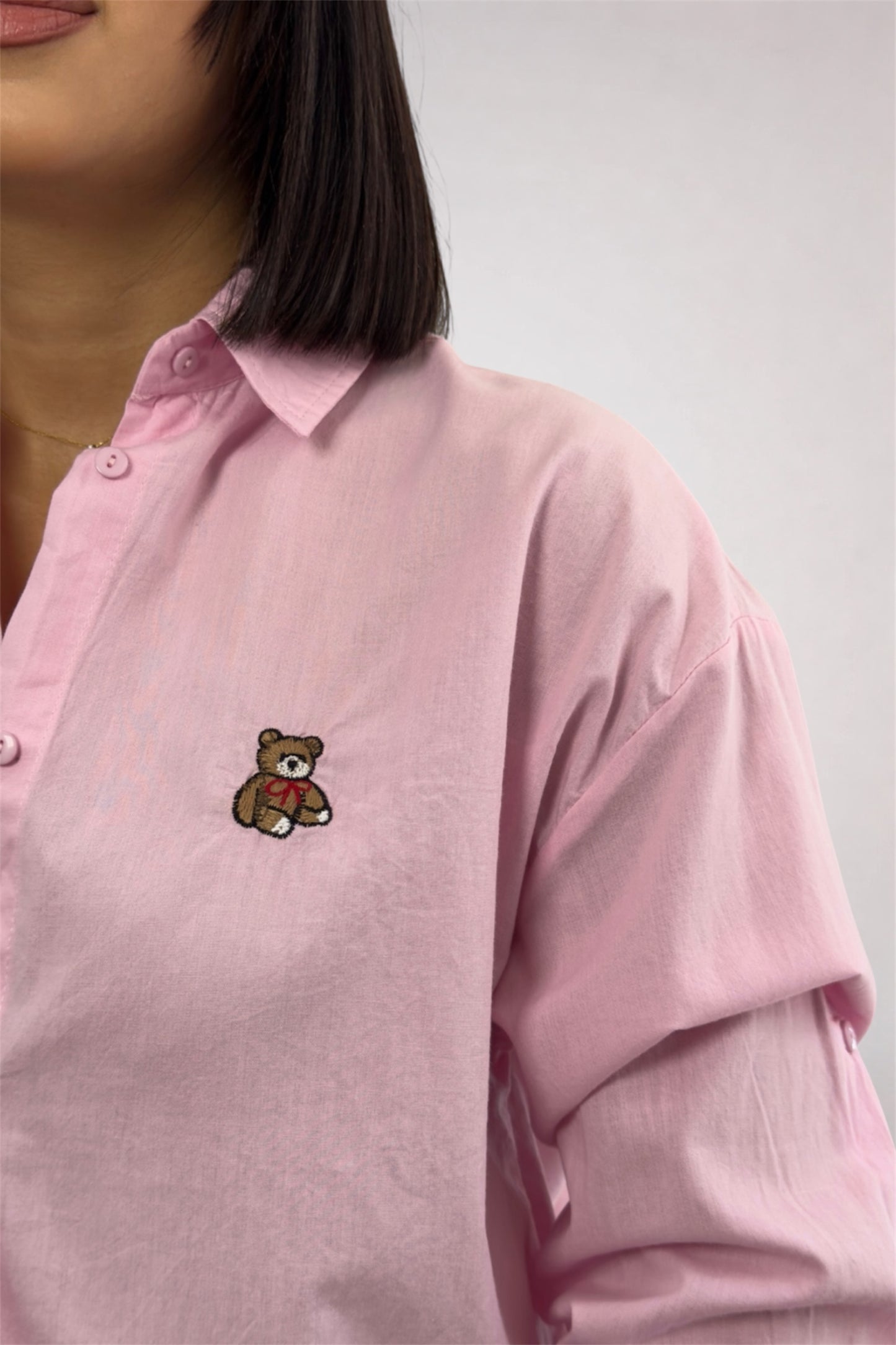 Pink shirt with a teddy bear emblem worn by a person on a plain background