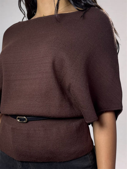 A close-up of a woman wearing a dark brown knit top with a wide boat neckline and short draped sleeves, styled with a thin black belt.