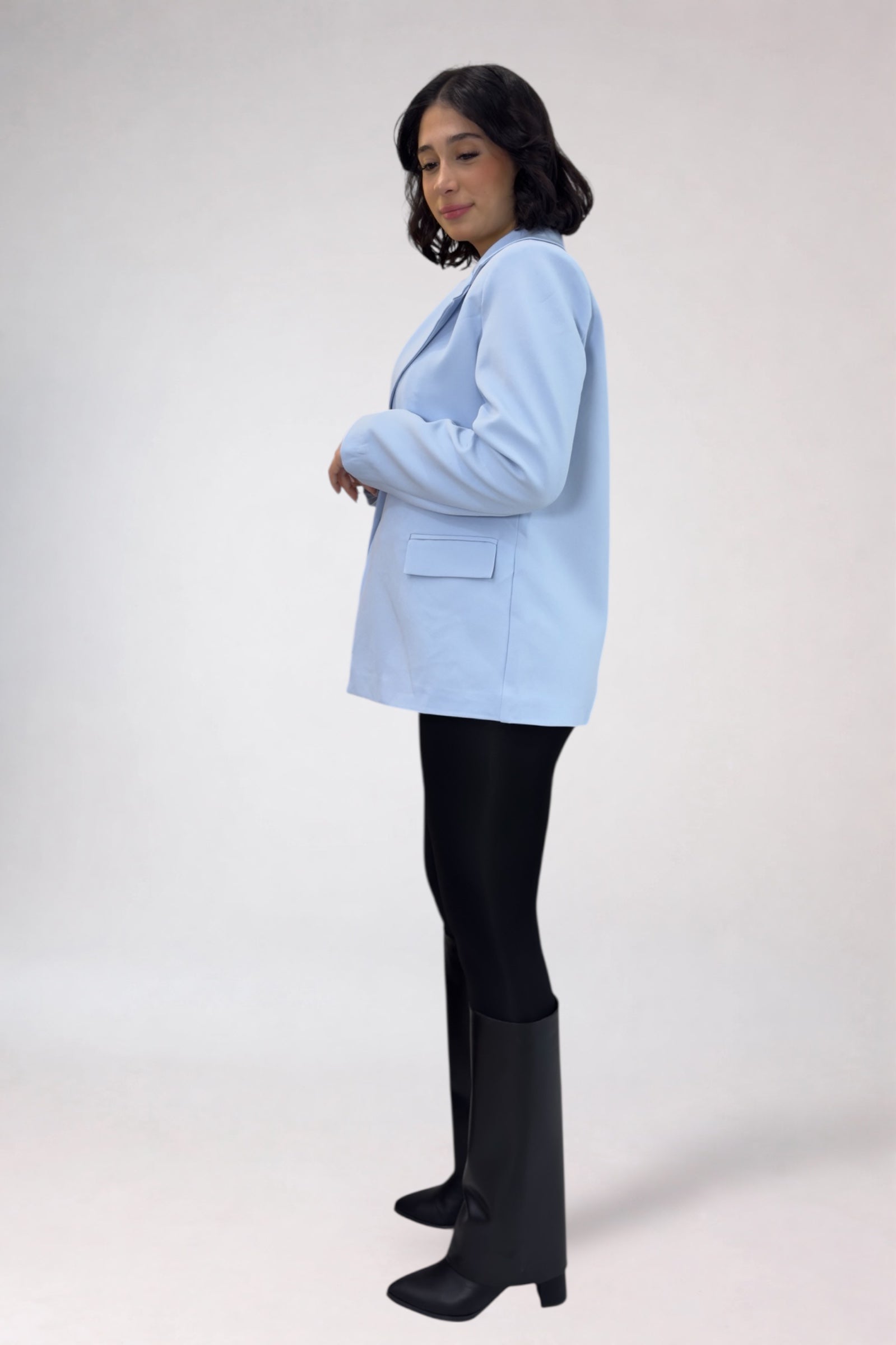 Woman wearing a light blue blazer, black pants, and black boots on a white background
