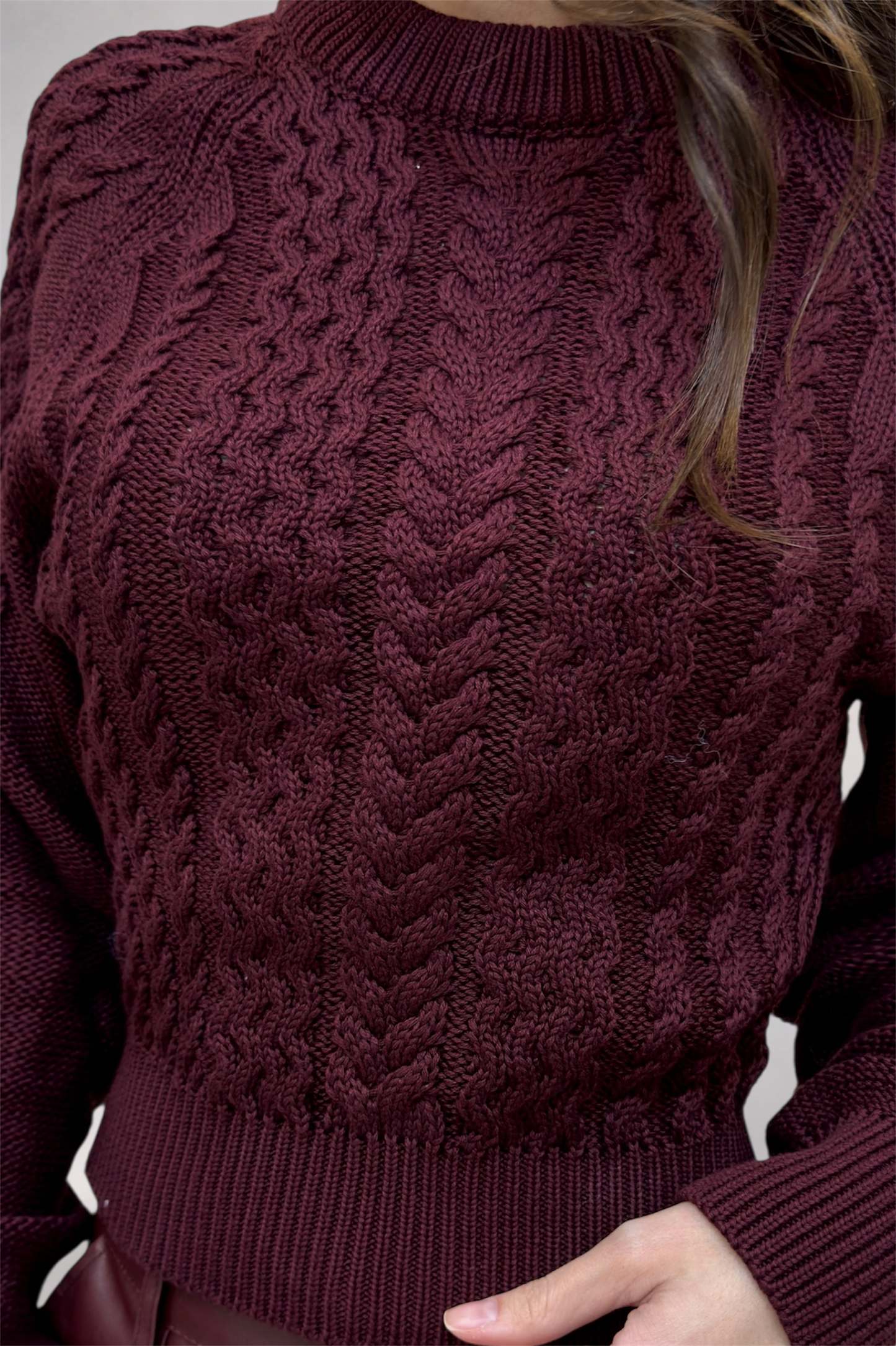 Close-up of a person wearing a cable knit burgundy sweater.