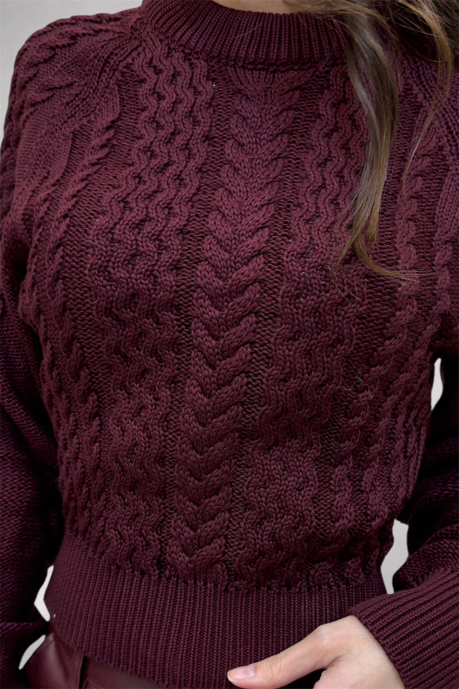 Close-up of a person wearing a cable knit burgundy sweater.