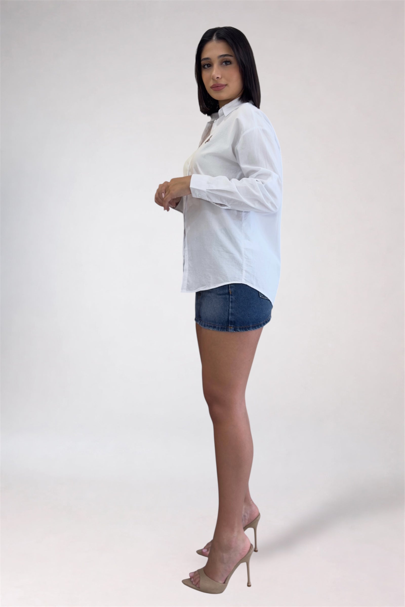 Woman wearing a white blouse and denim shorts on a plain background