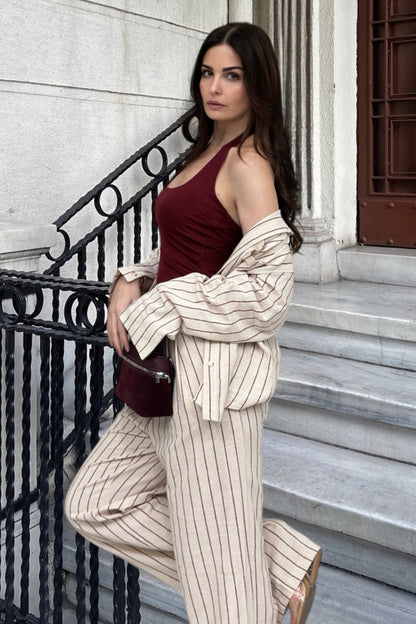 Woman in a burgundy top and beige striped pants standing on steps with a black railing.