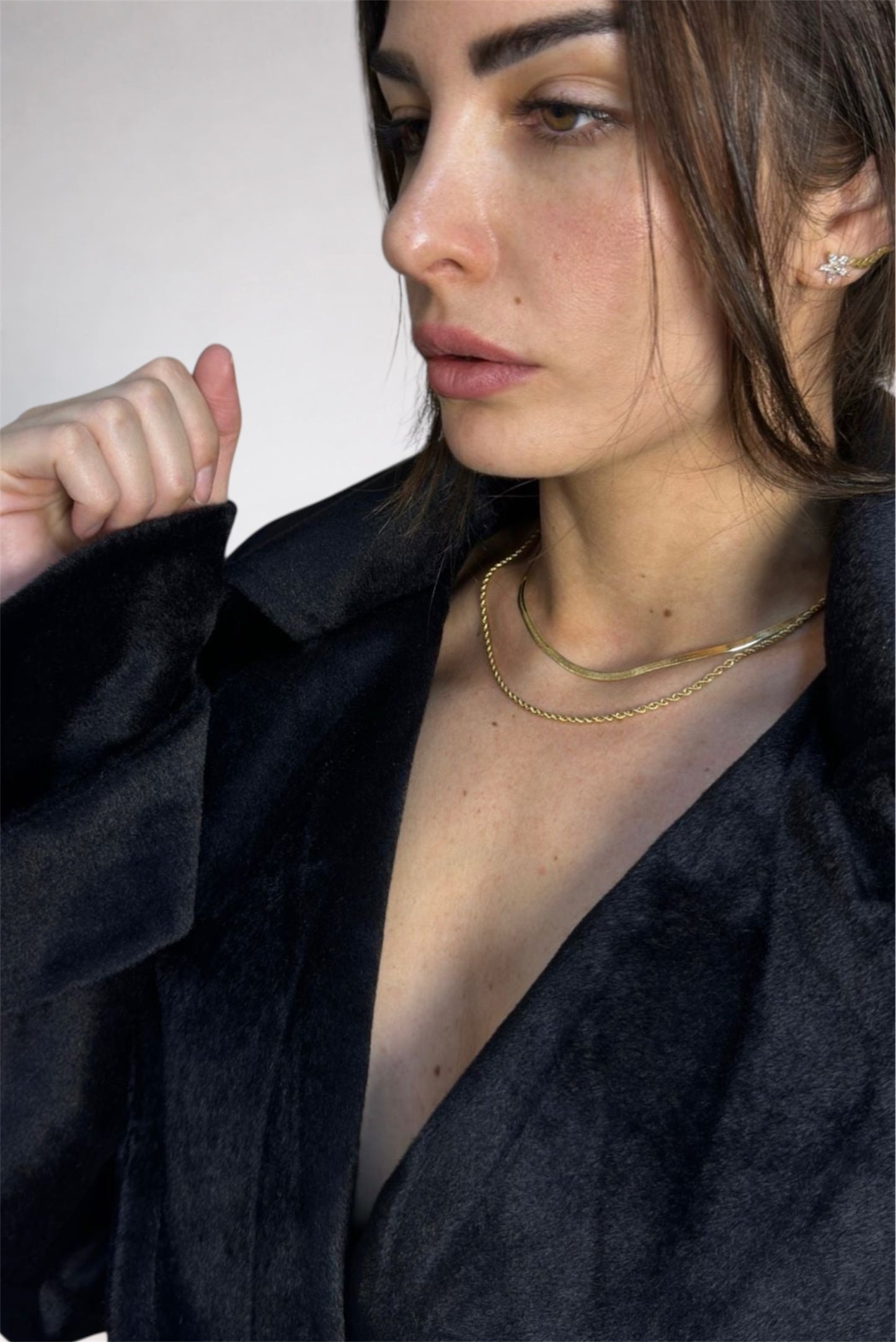 Woman wearing a black jacket and gold necklace against a white background