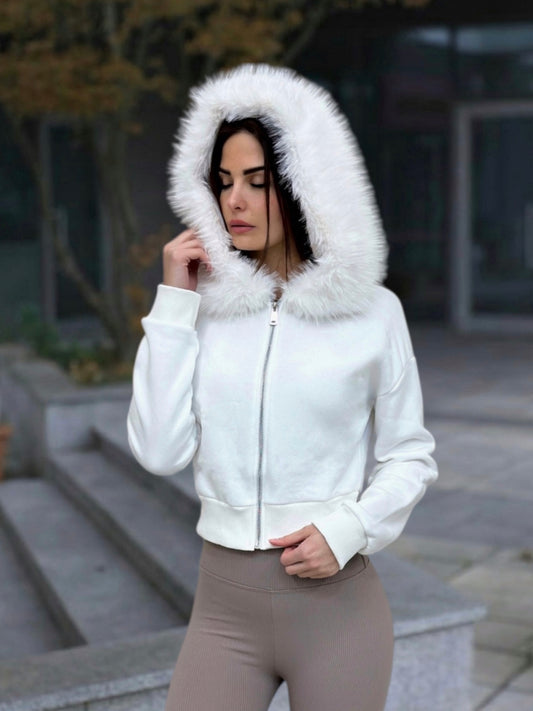 Woman wearing a white jacket with a fur-lined hood outdoors.