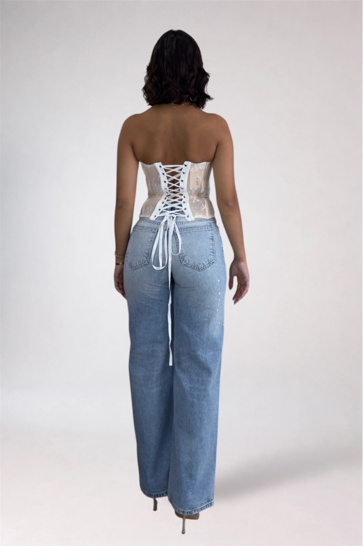 Person wearing a lace-up top and denim pants on a plain background
