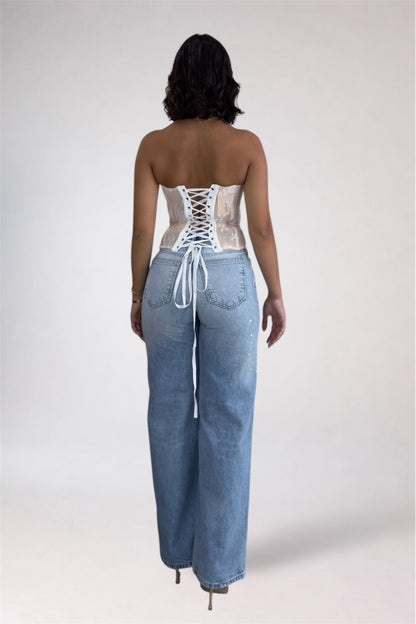 Person wearing a lace-up top and denim pants on a plain background