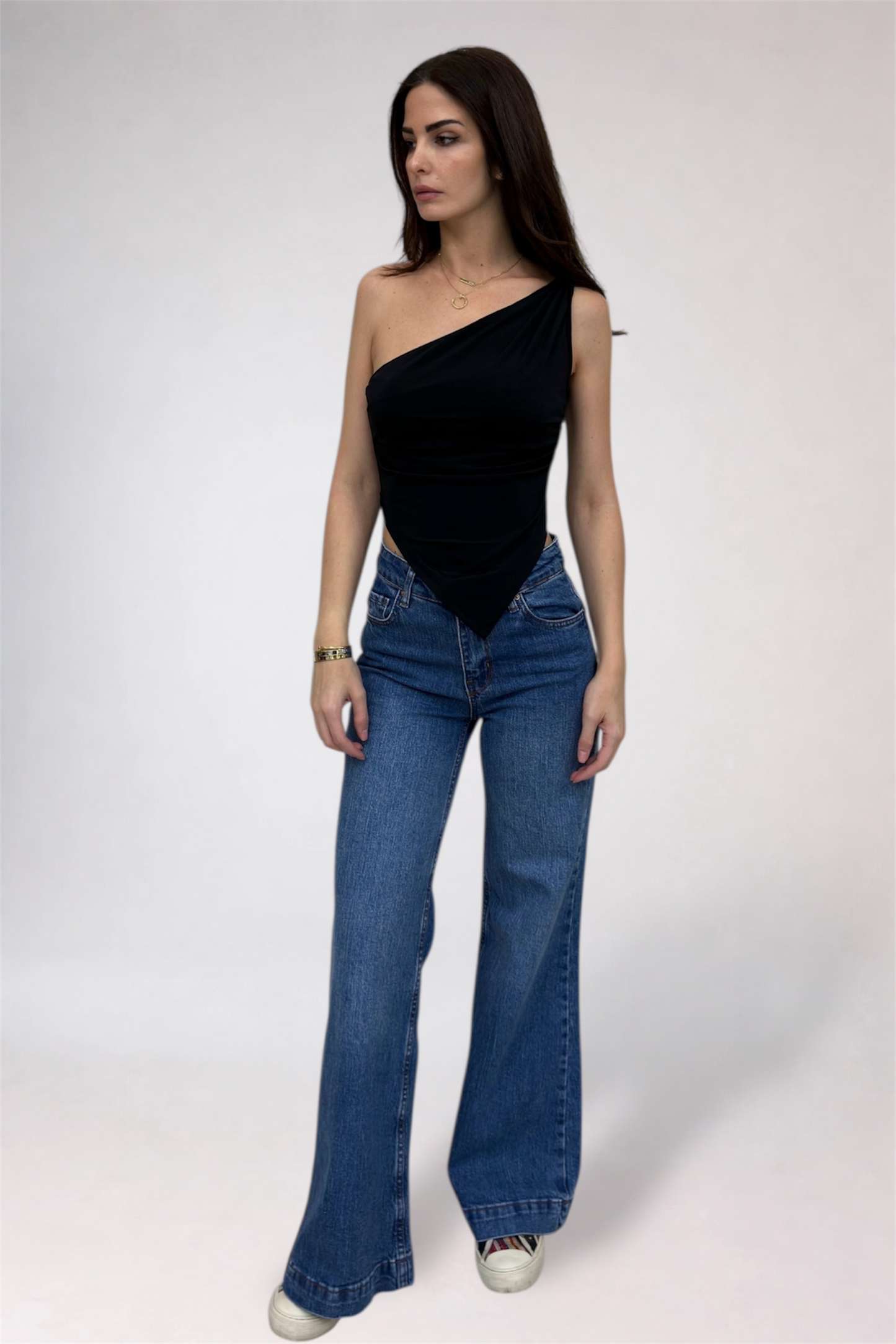 Woman wearing a black one-shoulder top and blue jeans on a white background