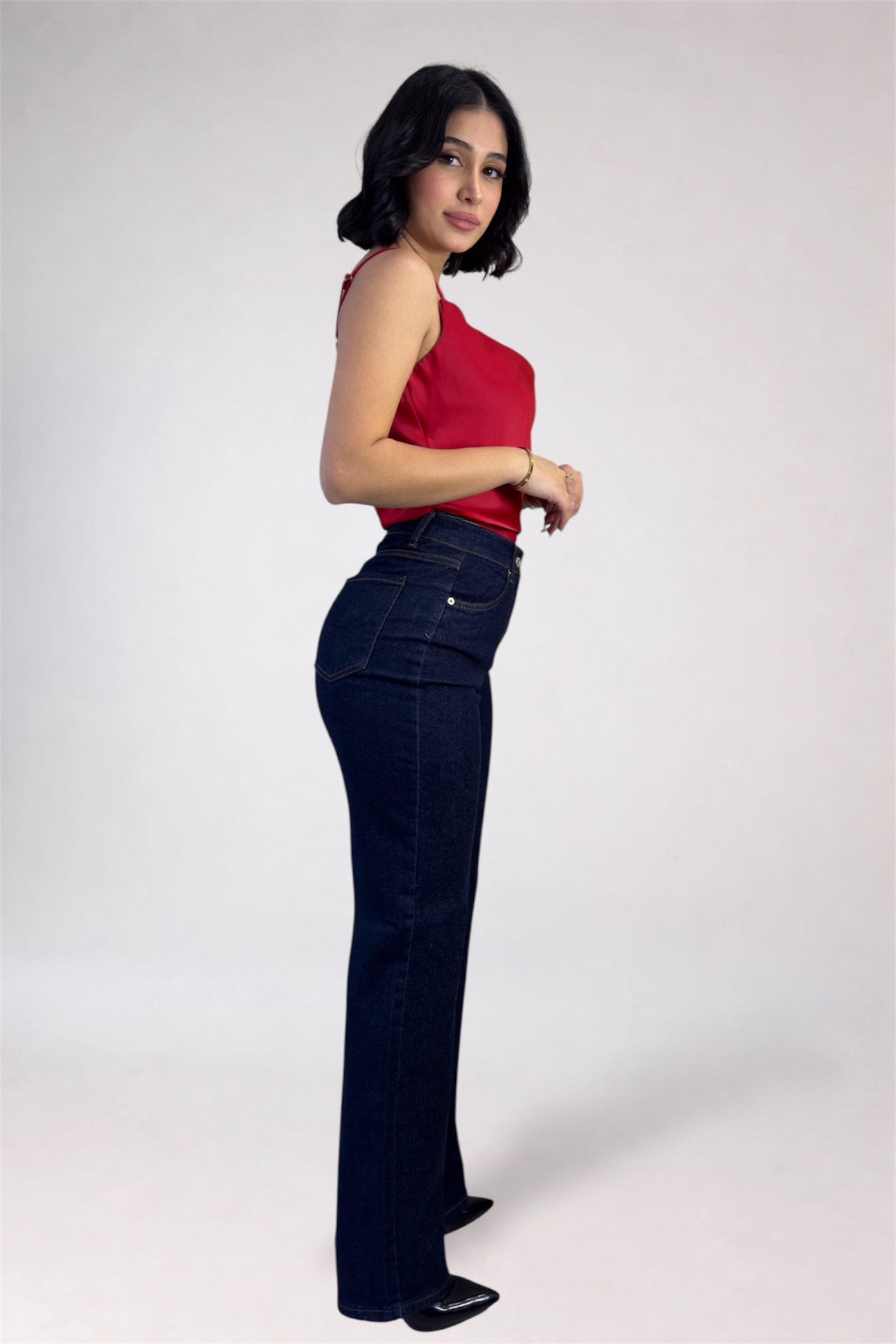 Woman wearing a red top and dark blue jeans on a white background