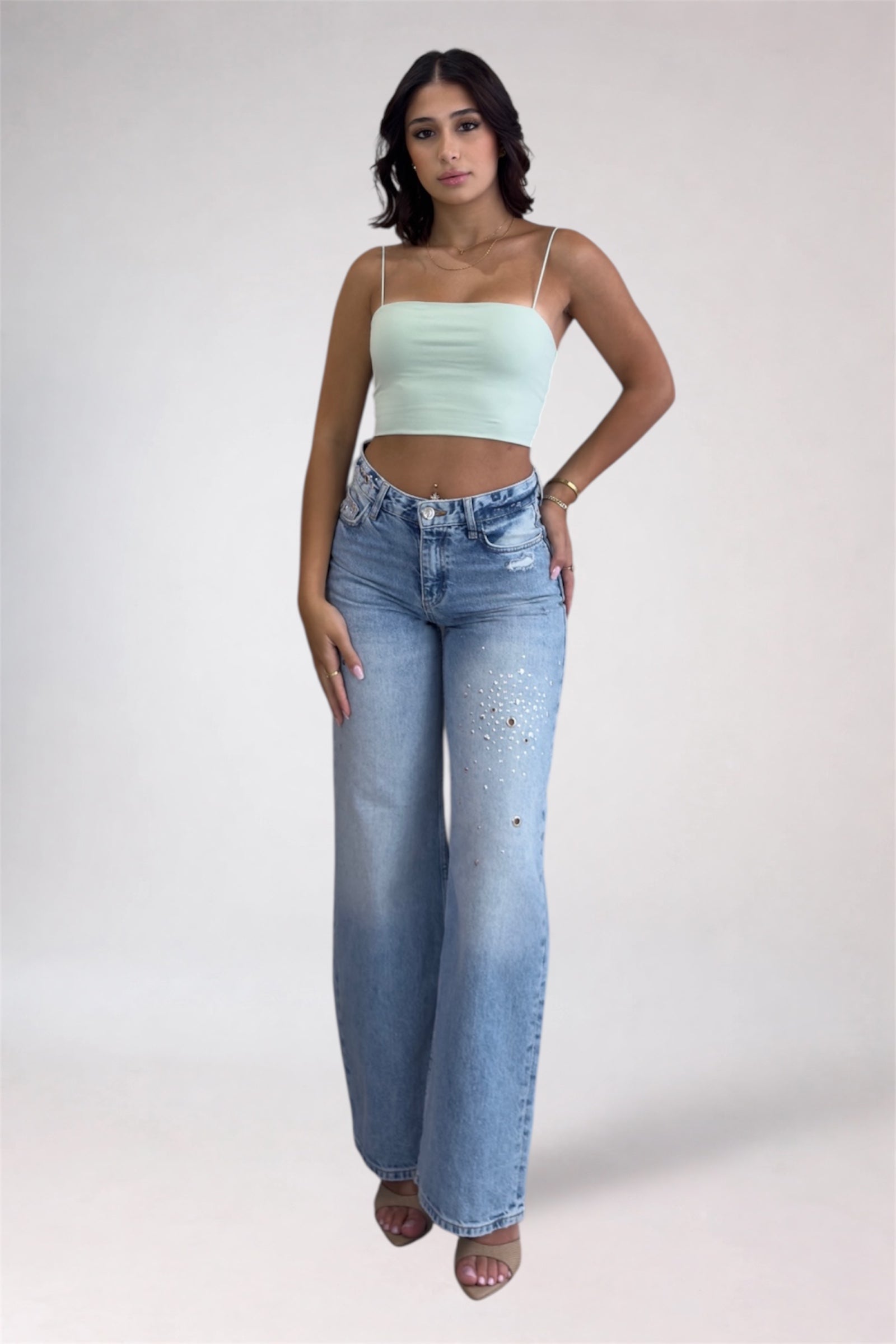 Woman wearing a light green top and blue jeans on a white background