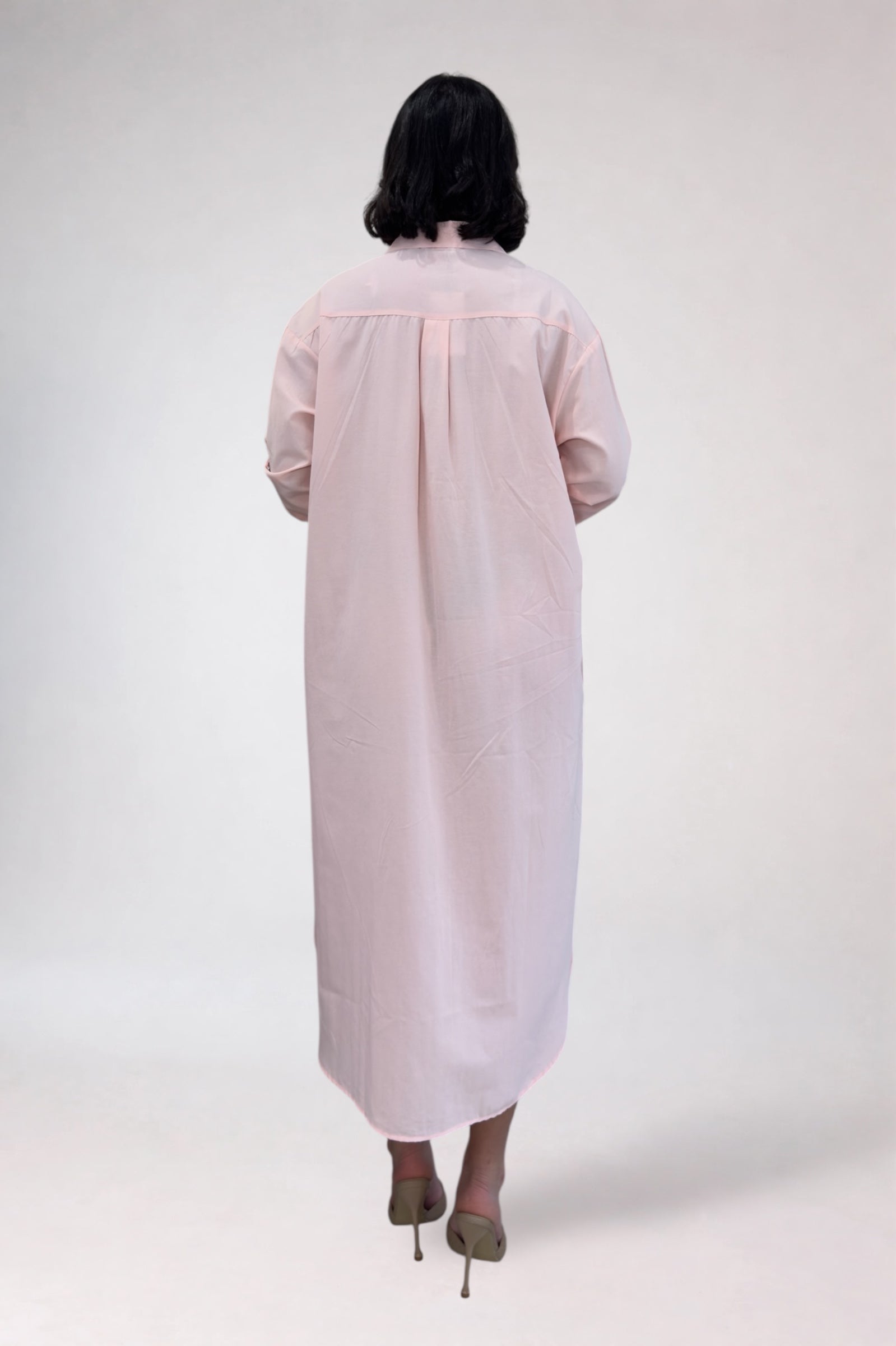 Person wearing a light pink dress with sheer sleeves on a white background