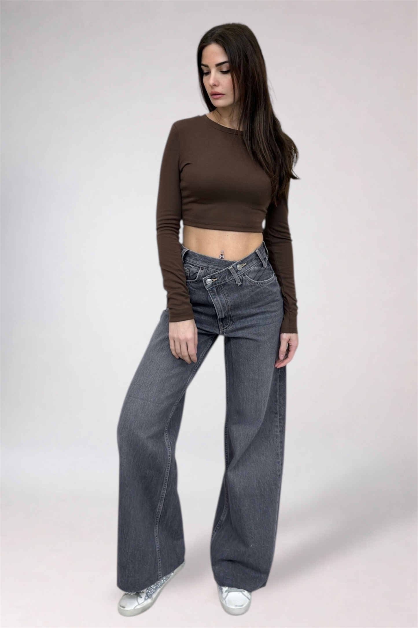 Woman wearing a brown long-sleeve top and gray jeans on a white background
