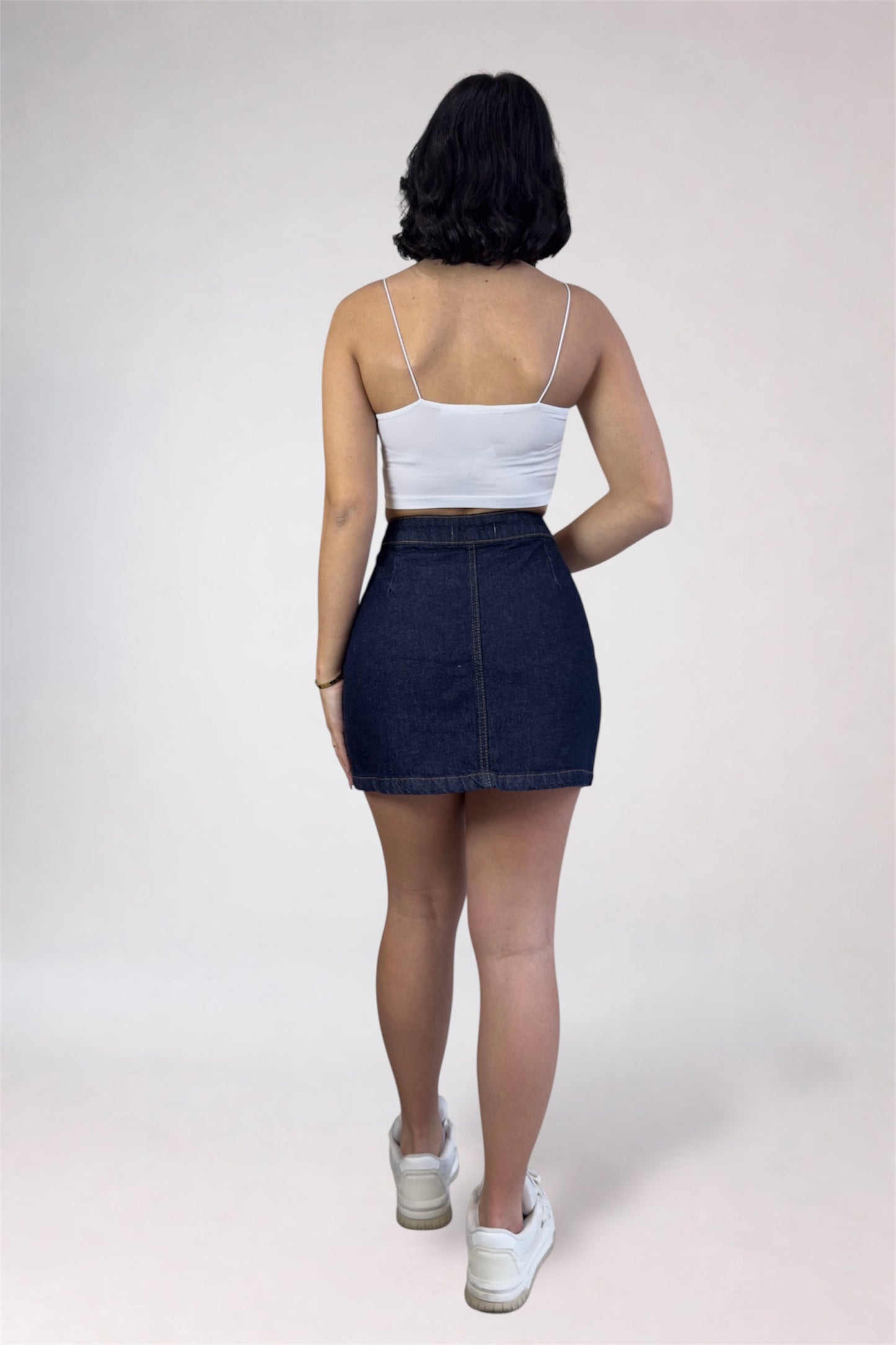 Person wearing a white crop top and dark denim skirt on a plain background
