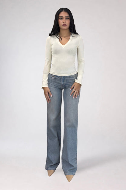 A woman modeling a cream long-sleeve V-neck top and light blue wide-leg jeans against a plain light gray studio background.