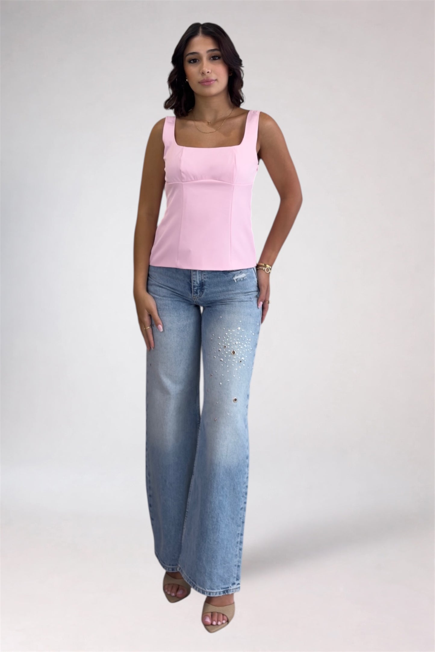 Woman wearing a pink tank top and blue jeans on a white background