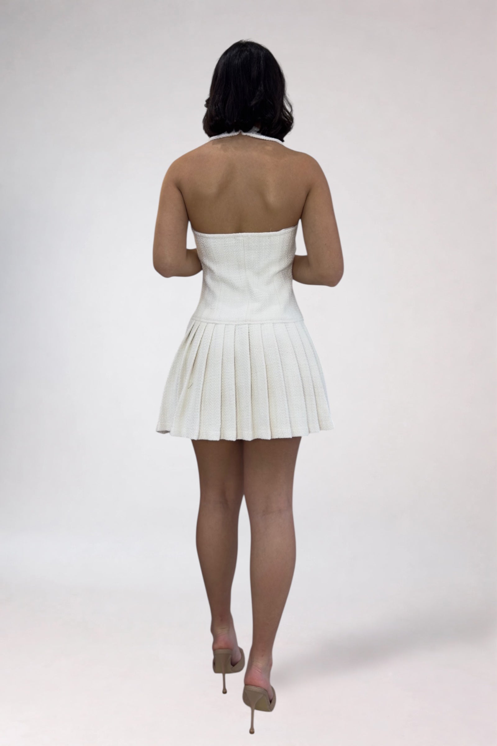 Person wearing a white pleated dress on a plain background