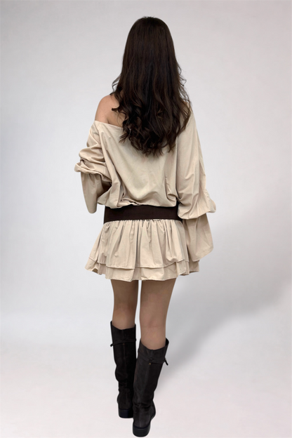 Woman wearing a beige off-shoulder top and skirt with black boots on a white background