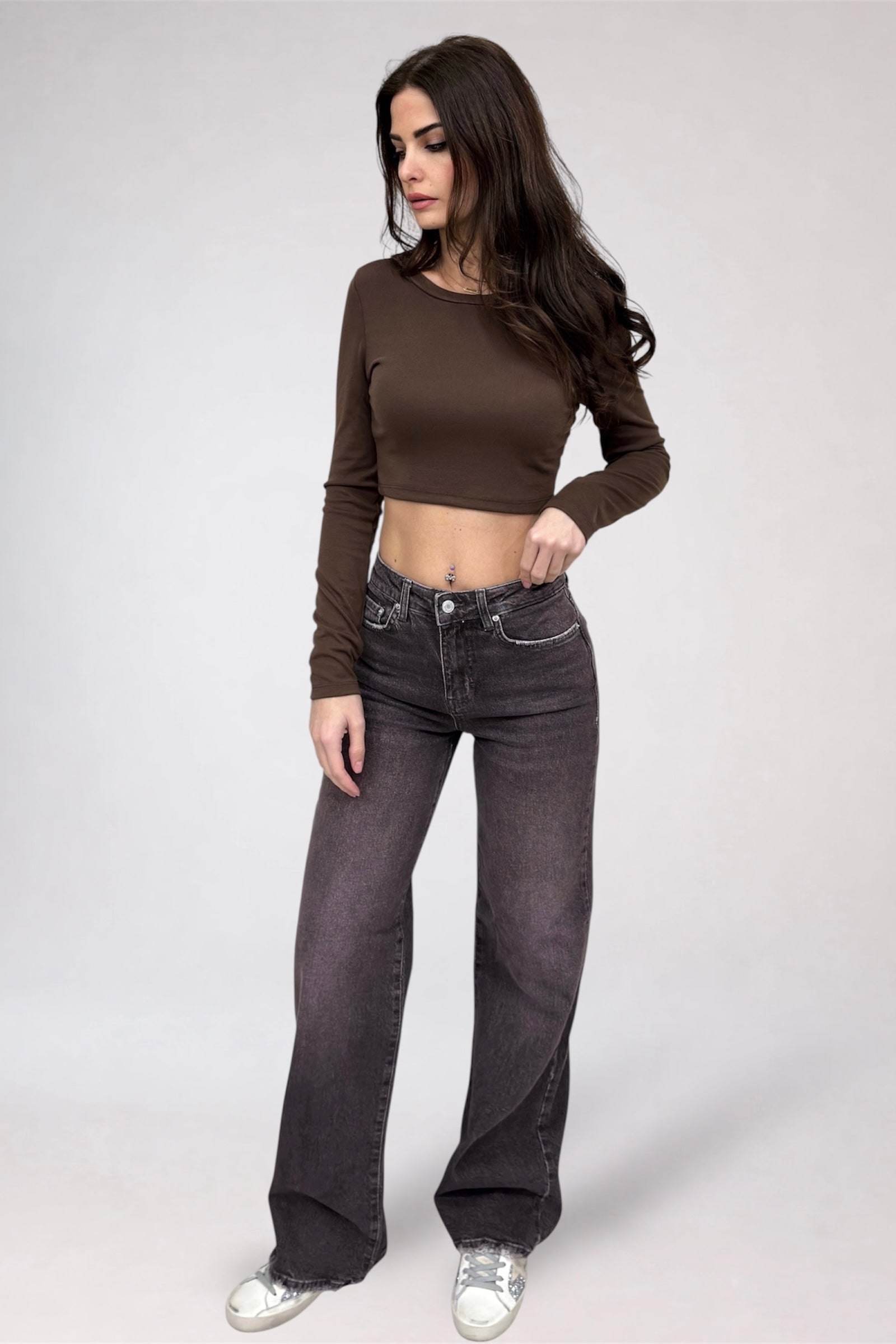 Woman wearing a brown long-sleeve top and dark jeans on a white background
