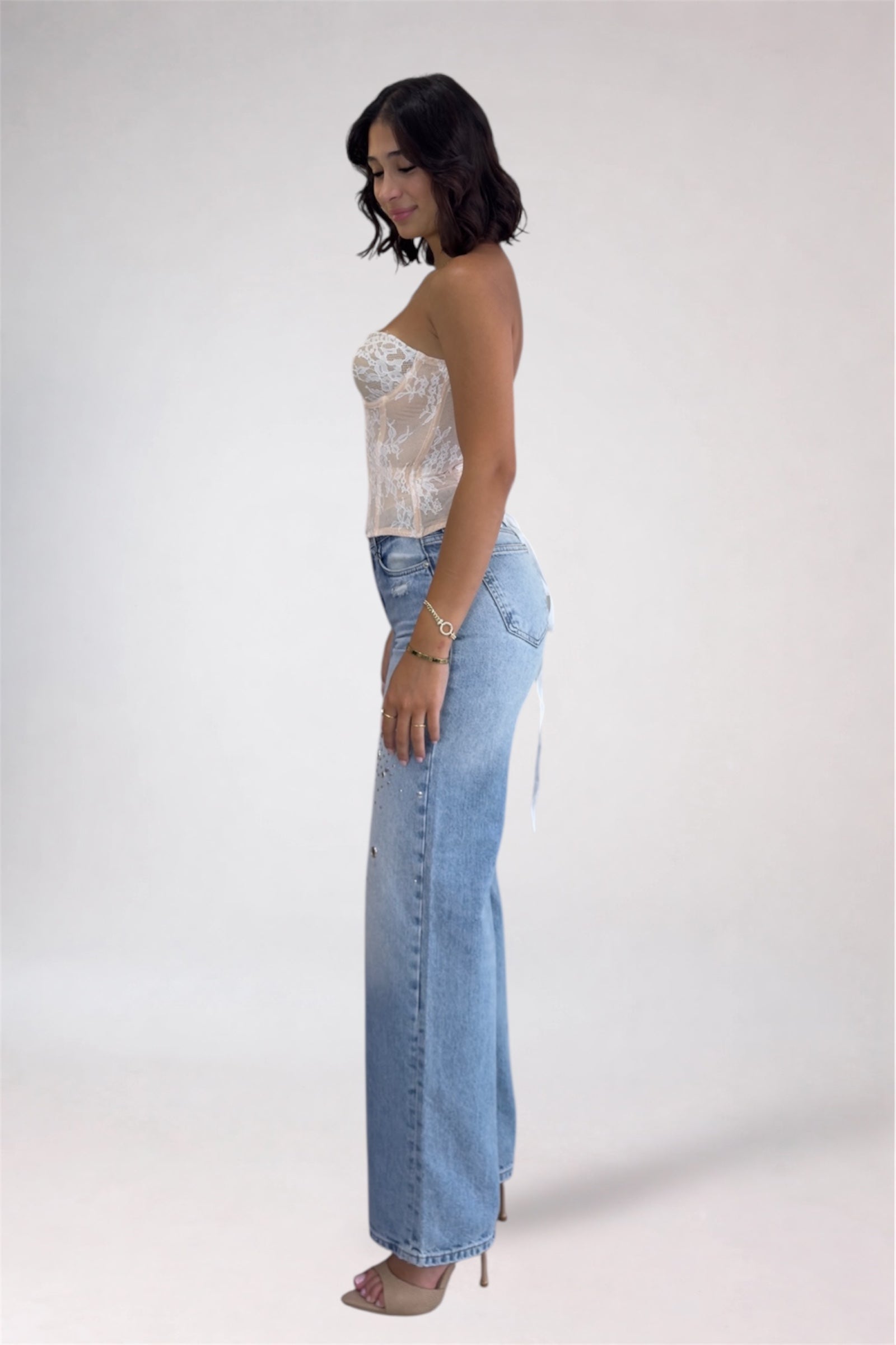 Woman wearing a white lace top and light blue jeans on a white background
