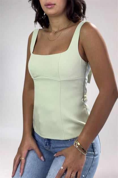 Woman wearing a light green tank top and blue jeans against a plain background