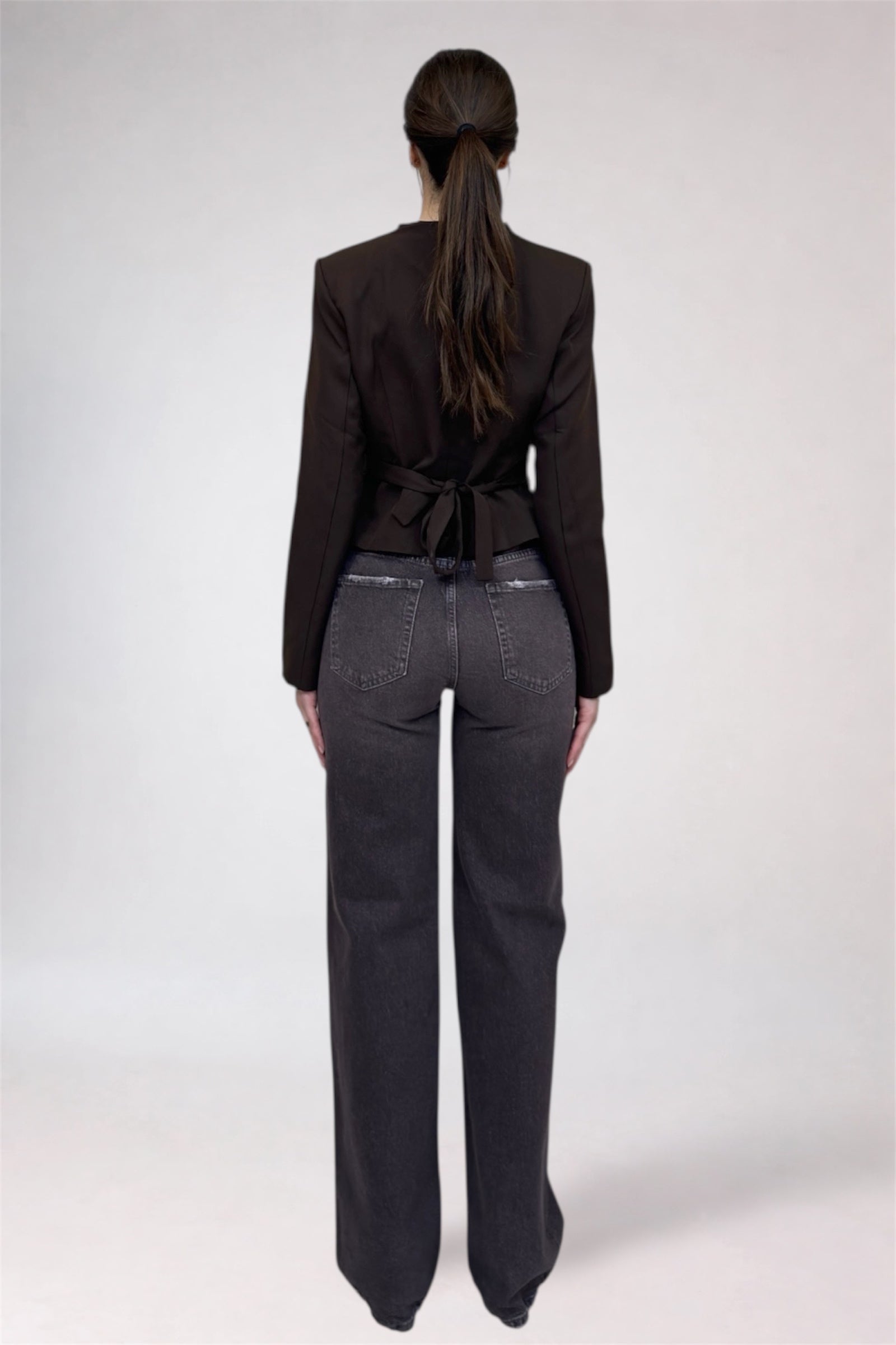 Person wearing a black blazer and dark jeans from behind on a white background