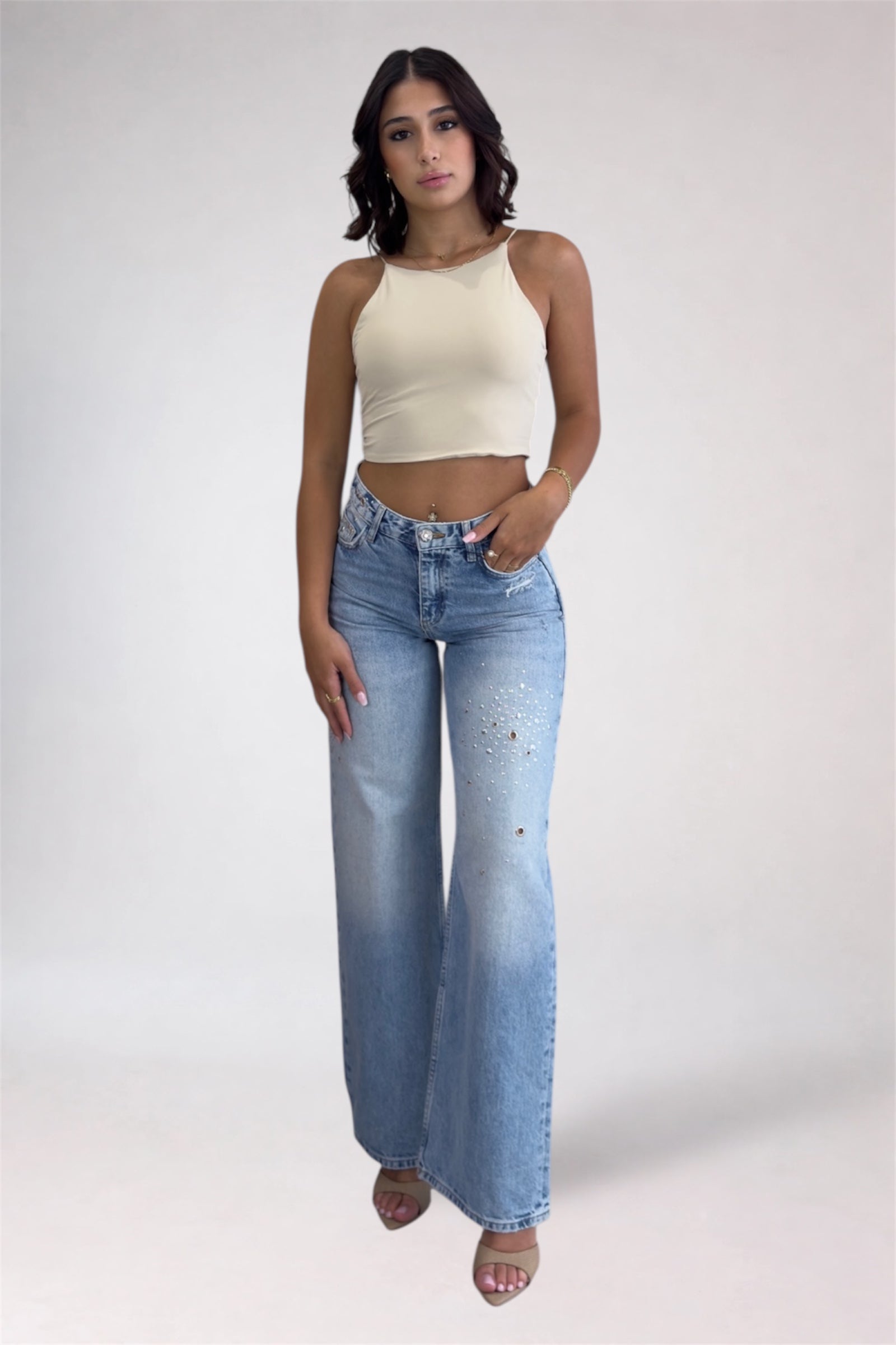 Woman wearing a beige top and blue jeans on a white background