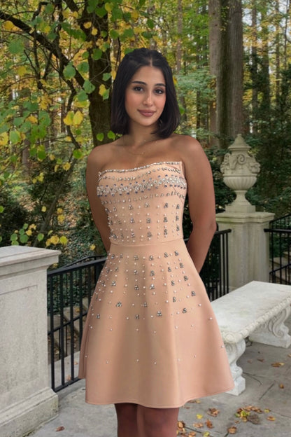 Woman in a beige strapless dress with embellishments standing outdoors in a garden setting.